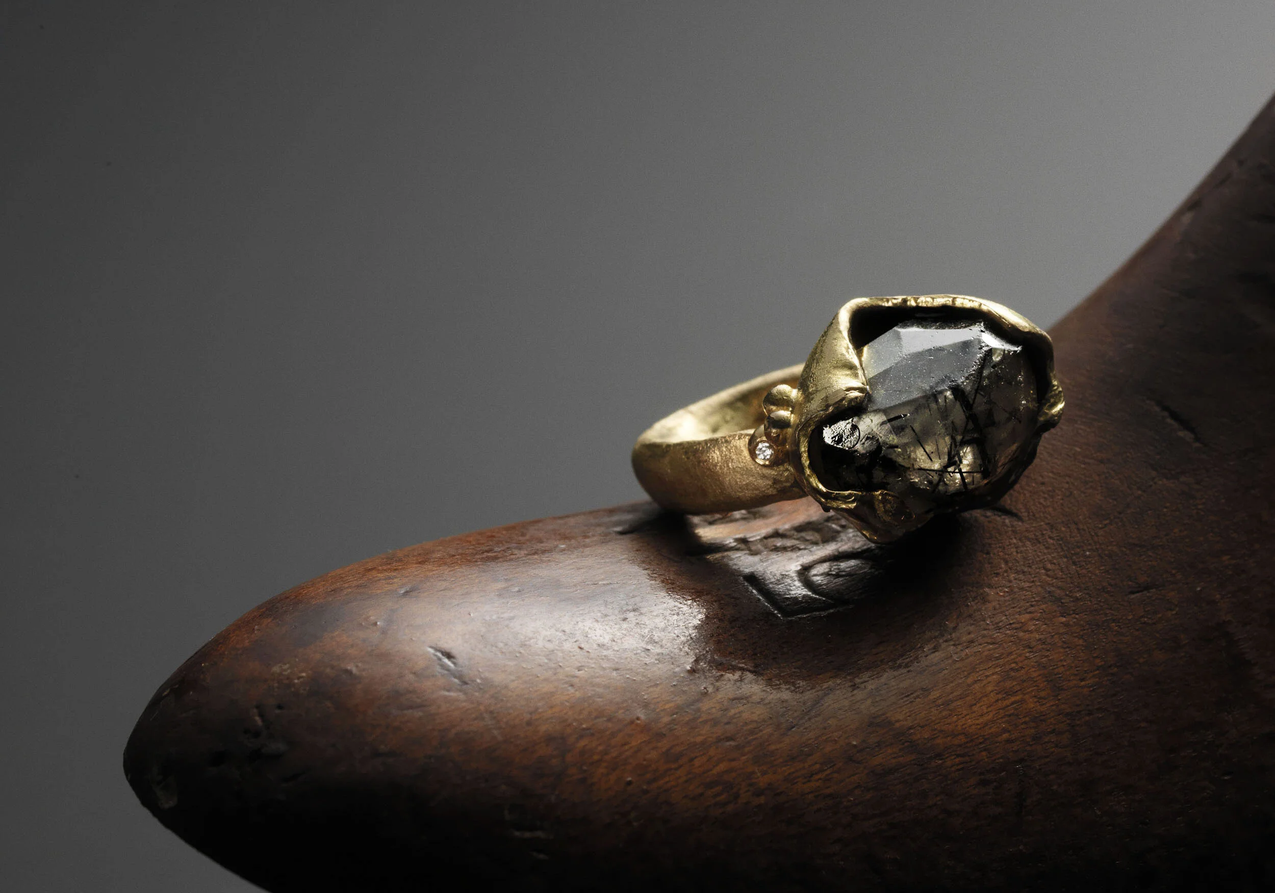 A ring with a large black gemstone and smaller diamonds on a wooden surface against a dark background.