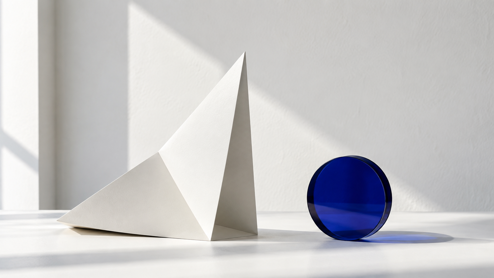 A sculptural white paper form and cobalt glass disc in soft natural light.