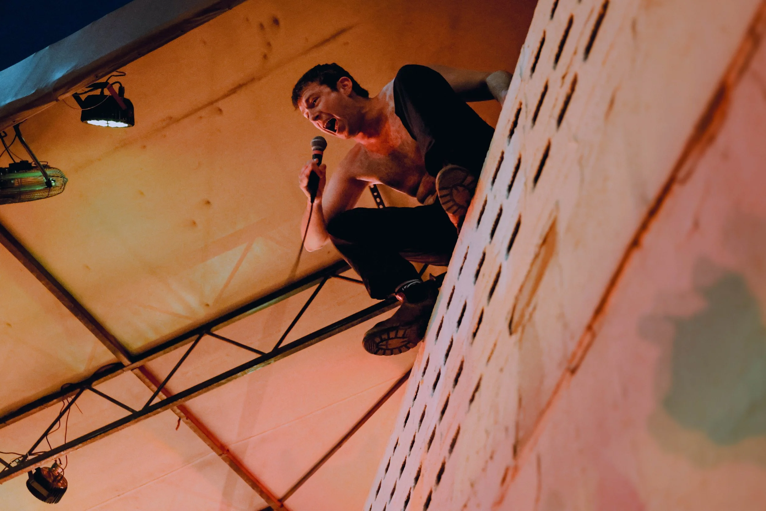 Charlie Steen of Shame (band) sings on top of a wall. 