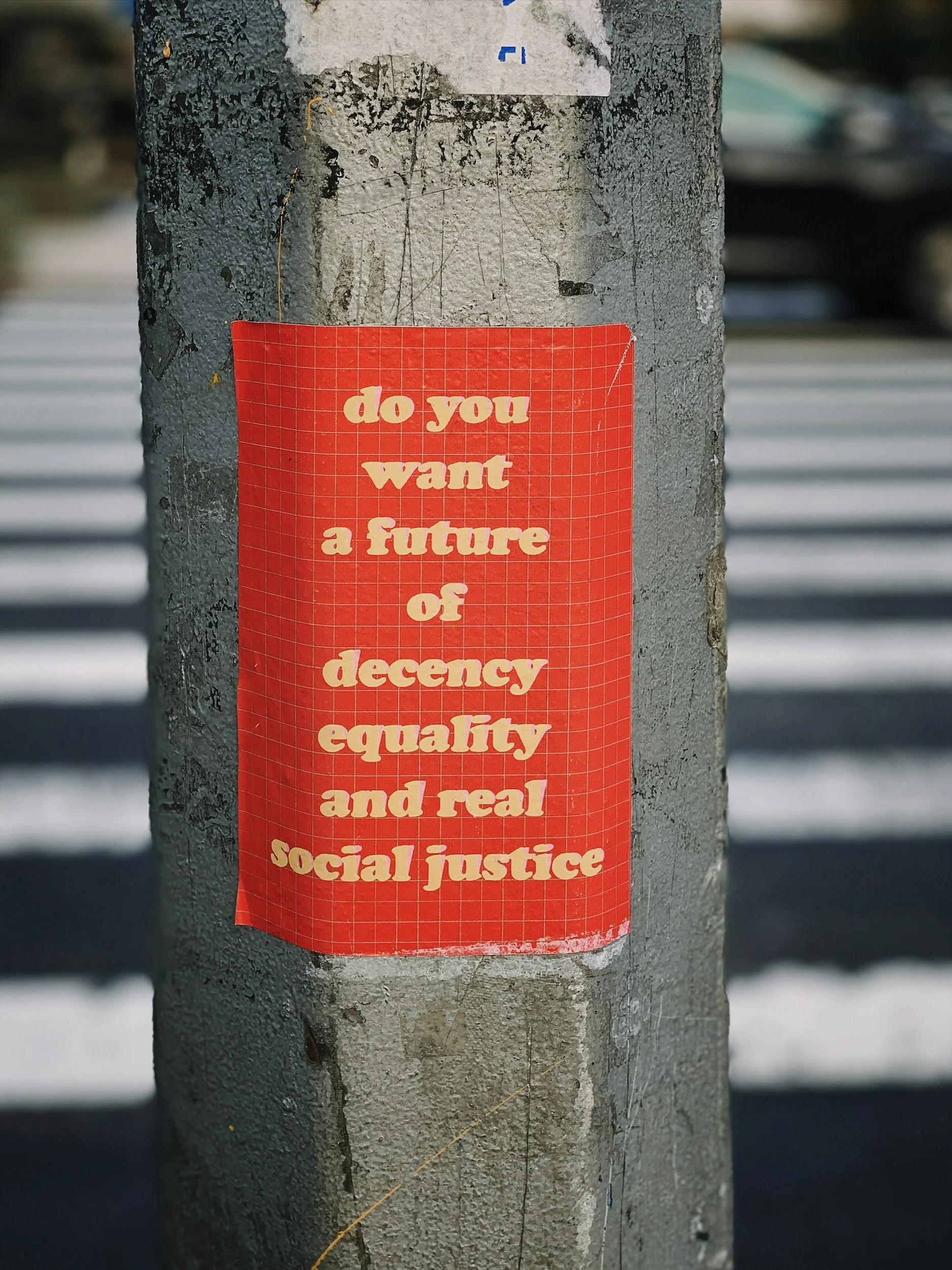 an image of a red sticker on a metal pole outside, the sticker says "do you want a future of decency equality and real social justice"