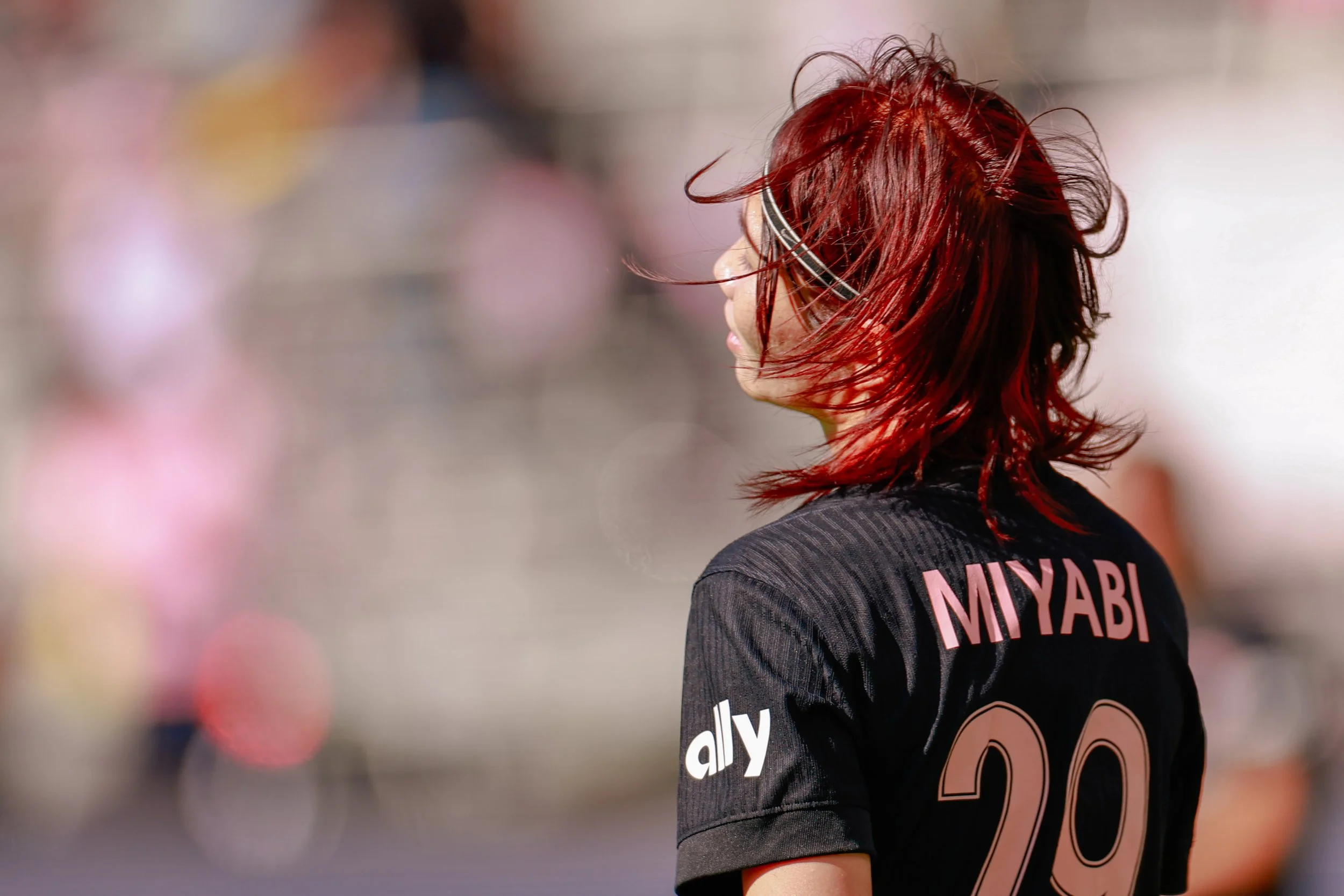 A woman with red hair wearing a black sports jersey with pink lettering that says "MIYABI" and the number 29. She is outdoors with a blurred background.