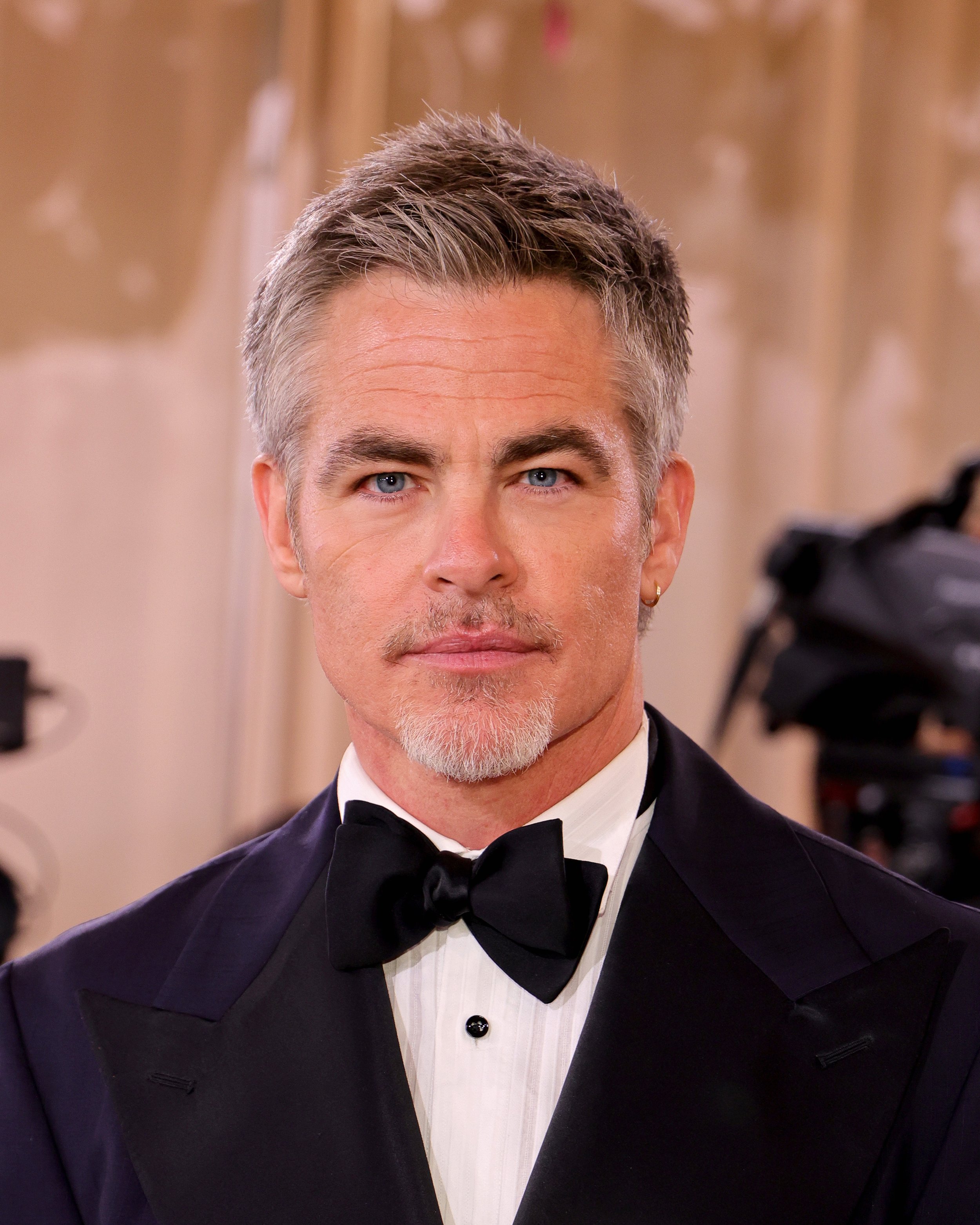 A man with short gray hair, blue eyes, and a goatee, dressed in a tuxedo with a black bow tie, looking directly at the camera at a formal event.