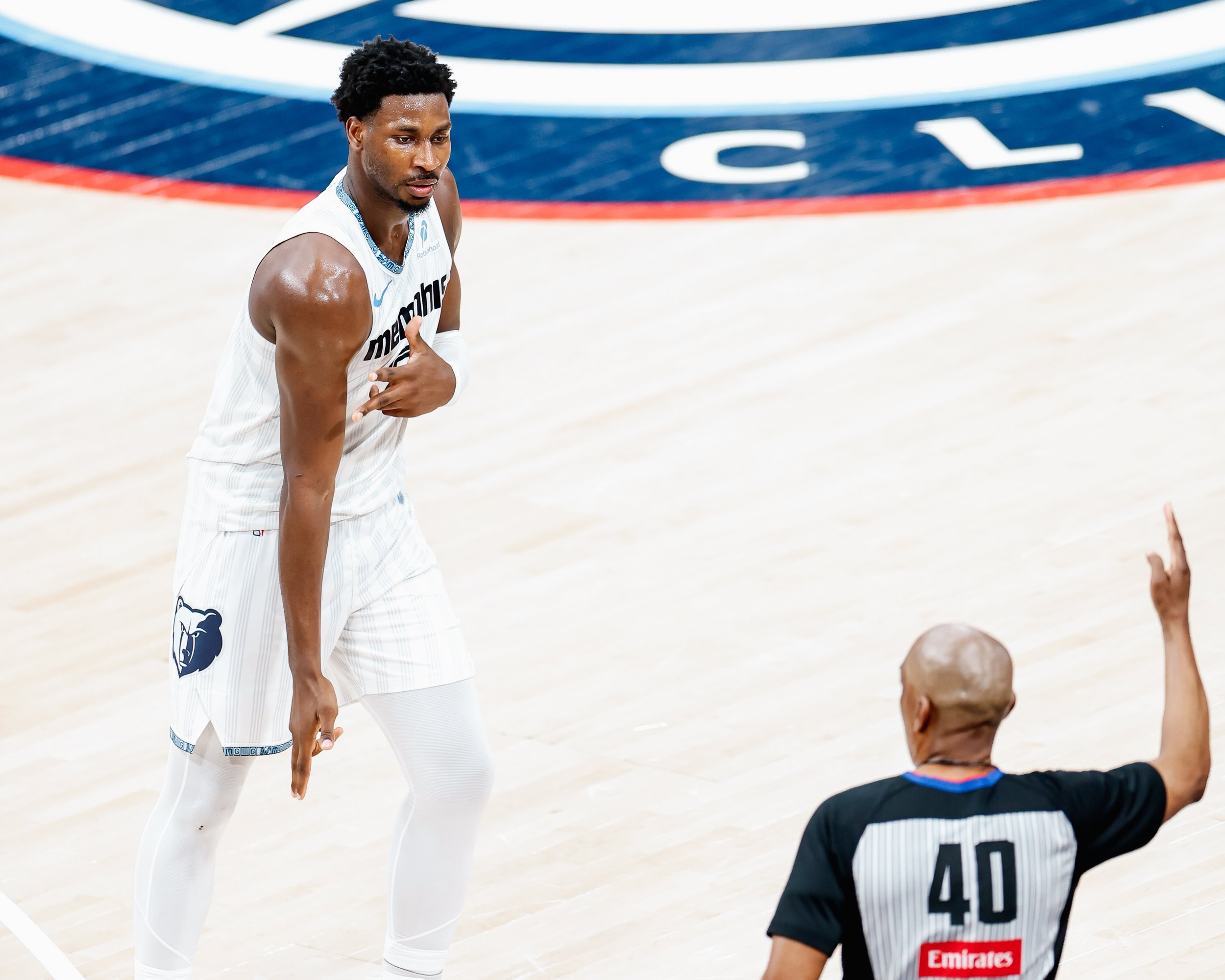 A basketball player in a Memphis Grizzlies uniform gestures towards a referee during a game.