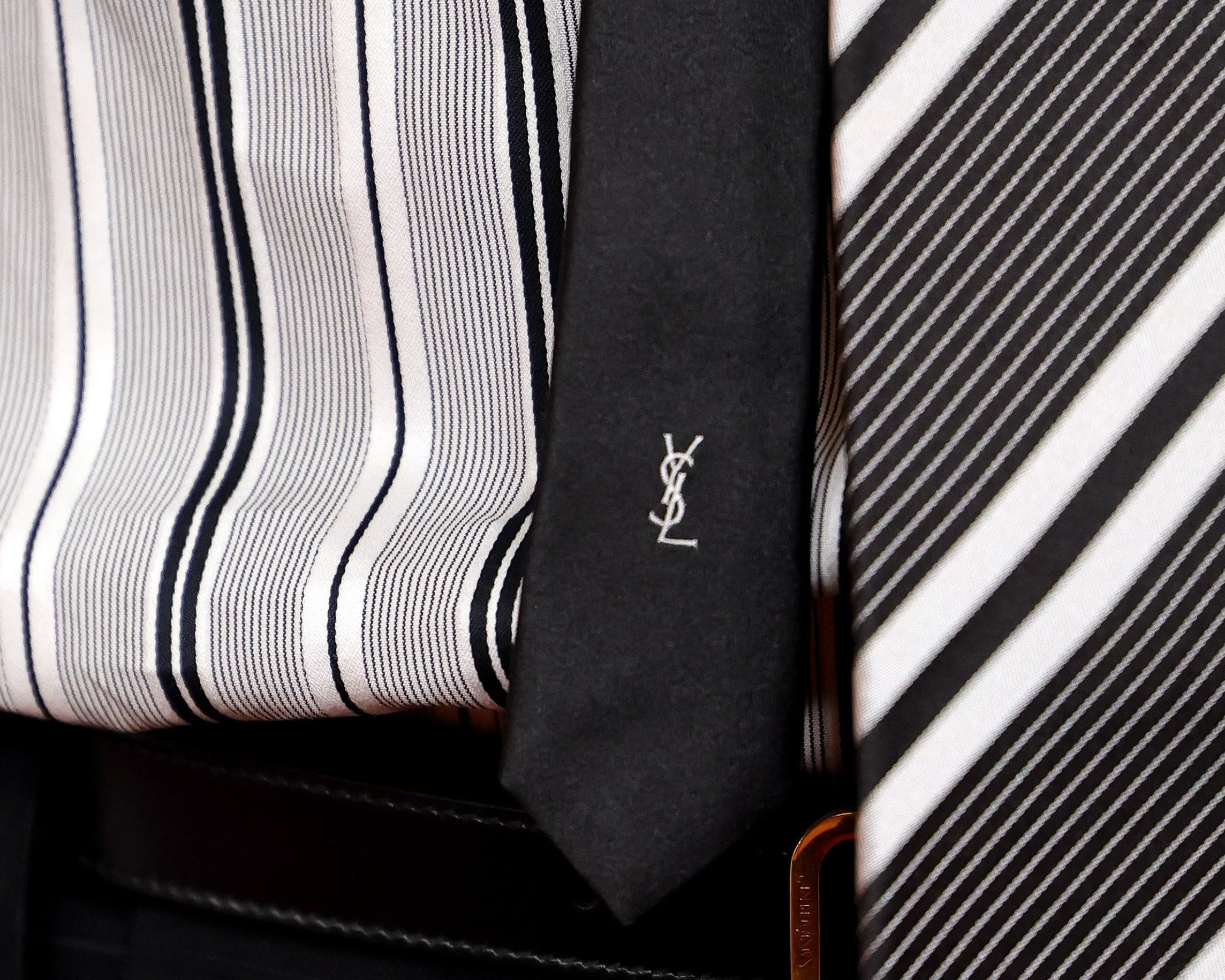 Close-up of a black Yves Saint Laurent tie and two pinstripe shirts, one with white and black stripes and the other with beige and black stripes.