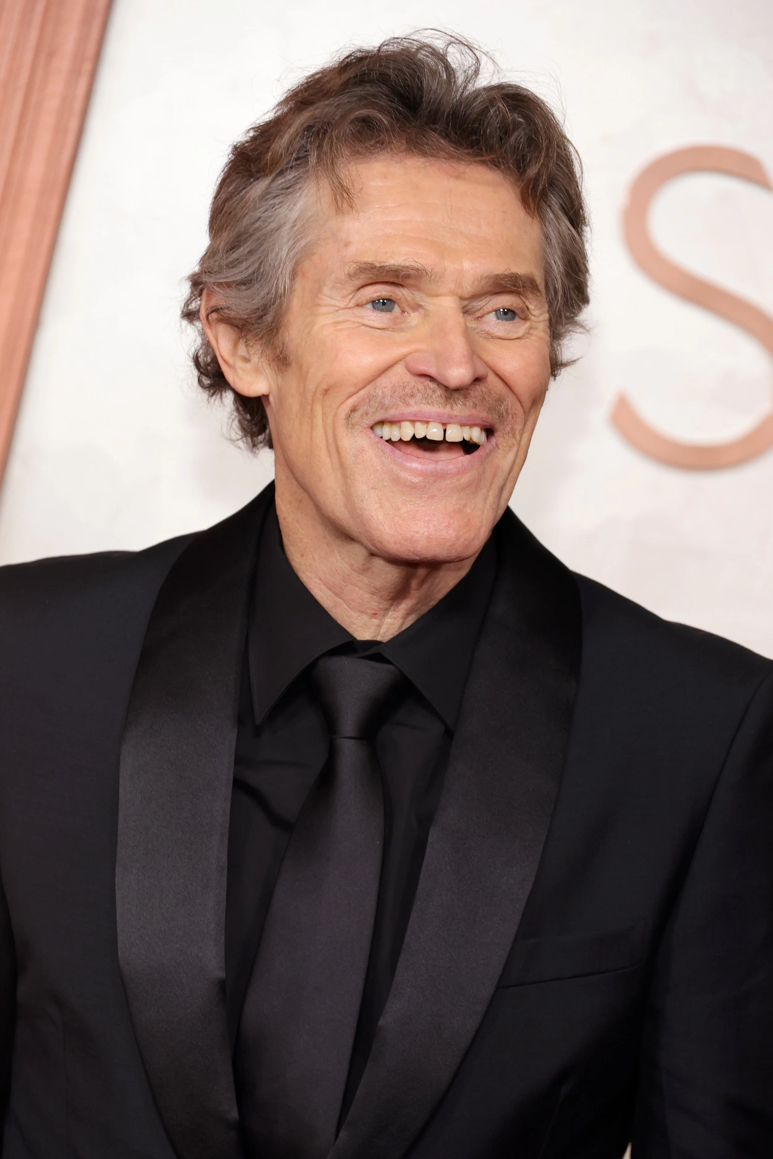 A smiling older man with gray hair wearing a black tuxedo and black tie at a formal event.