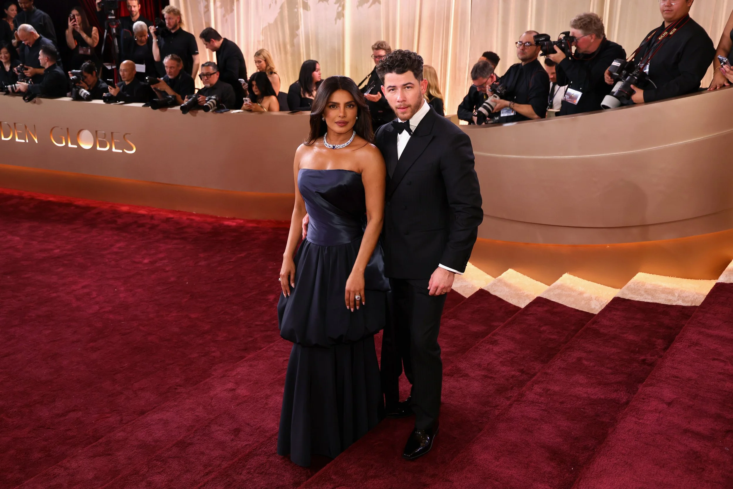A man and a woman posing on a red carpet at an awards event, with photographers and attendees in the background.