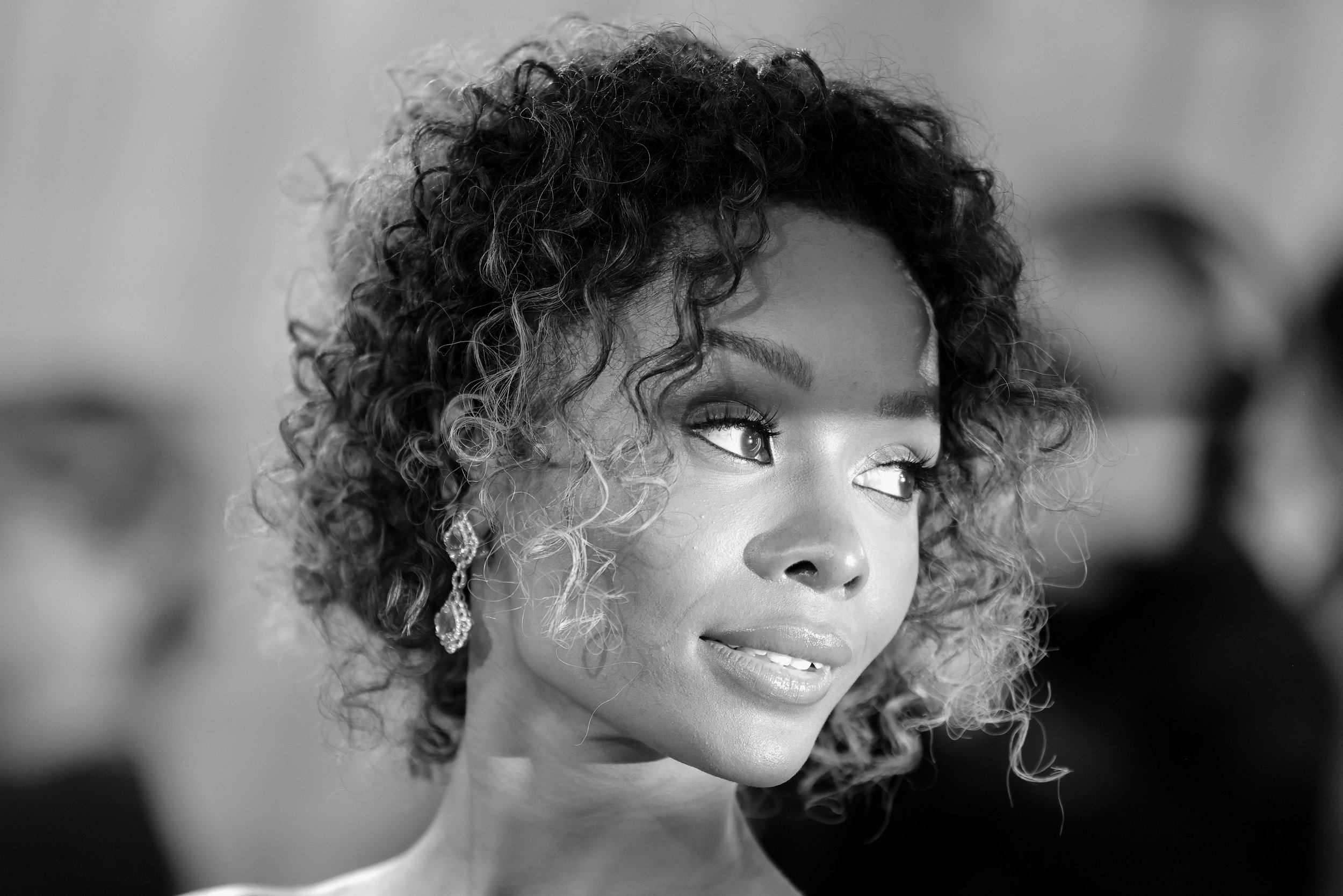Black and white photo of woman with curly hair wearing earrings, looking to the side.