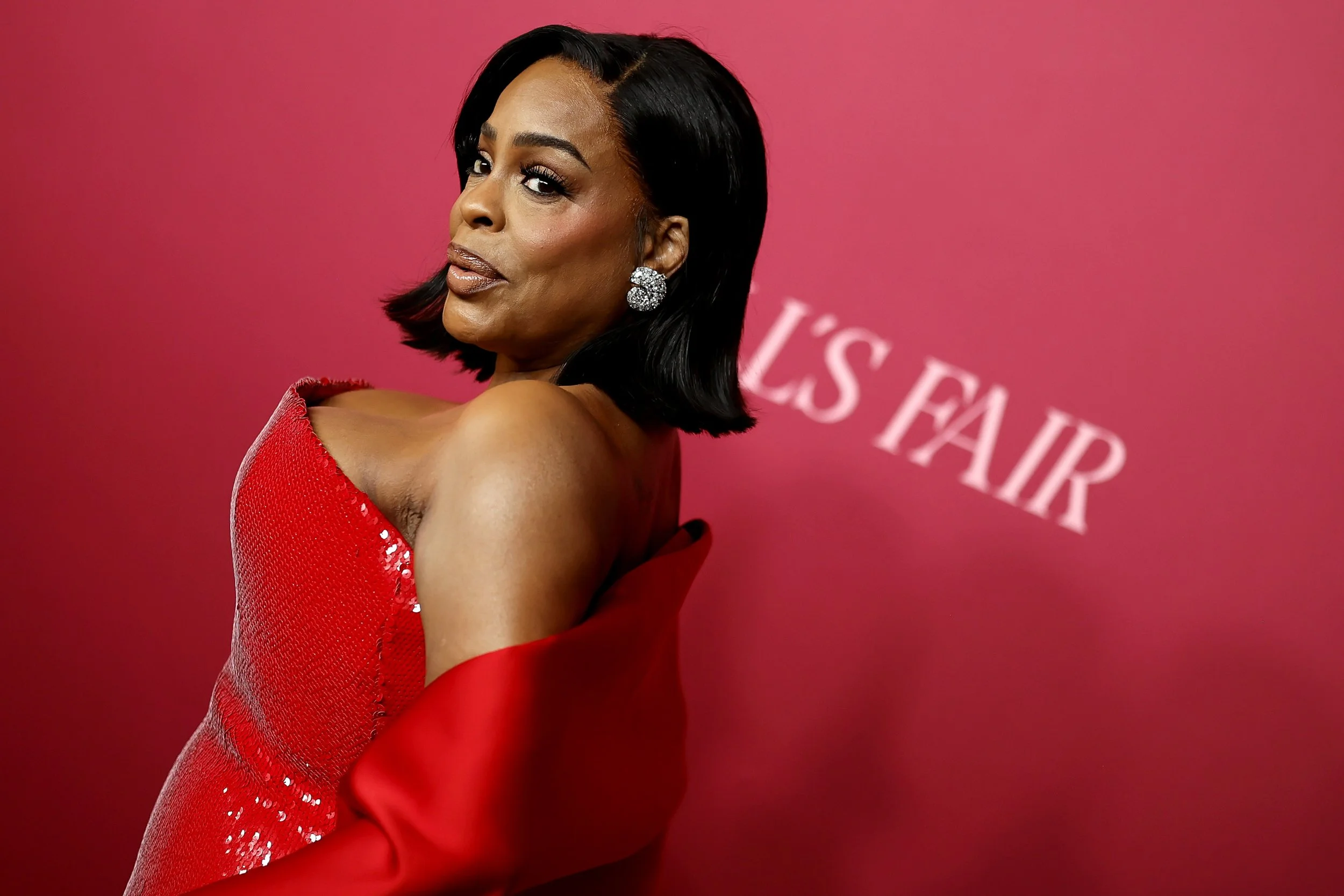 Woman in a red dress with one shoulder exposed, against a pink background with white text saying "GOLDEN GLOBES FAIR."