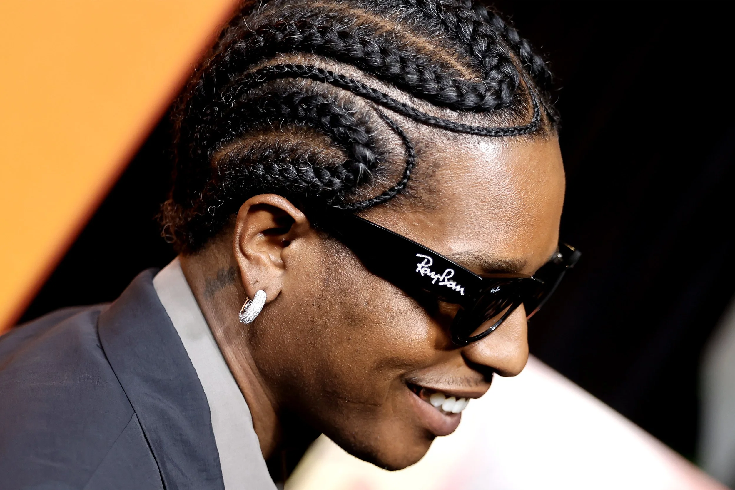 Close-up of a woman with braided hair, wearing sunglasses and hoop earrings, smiling.