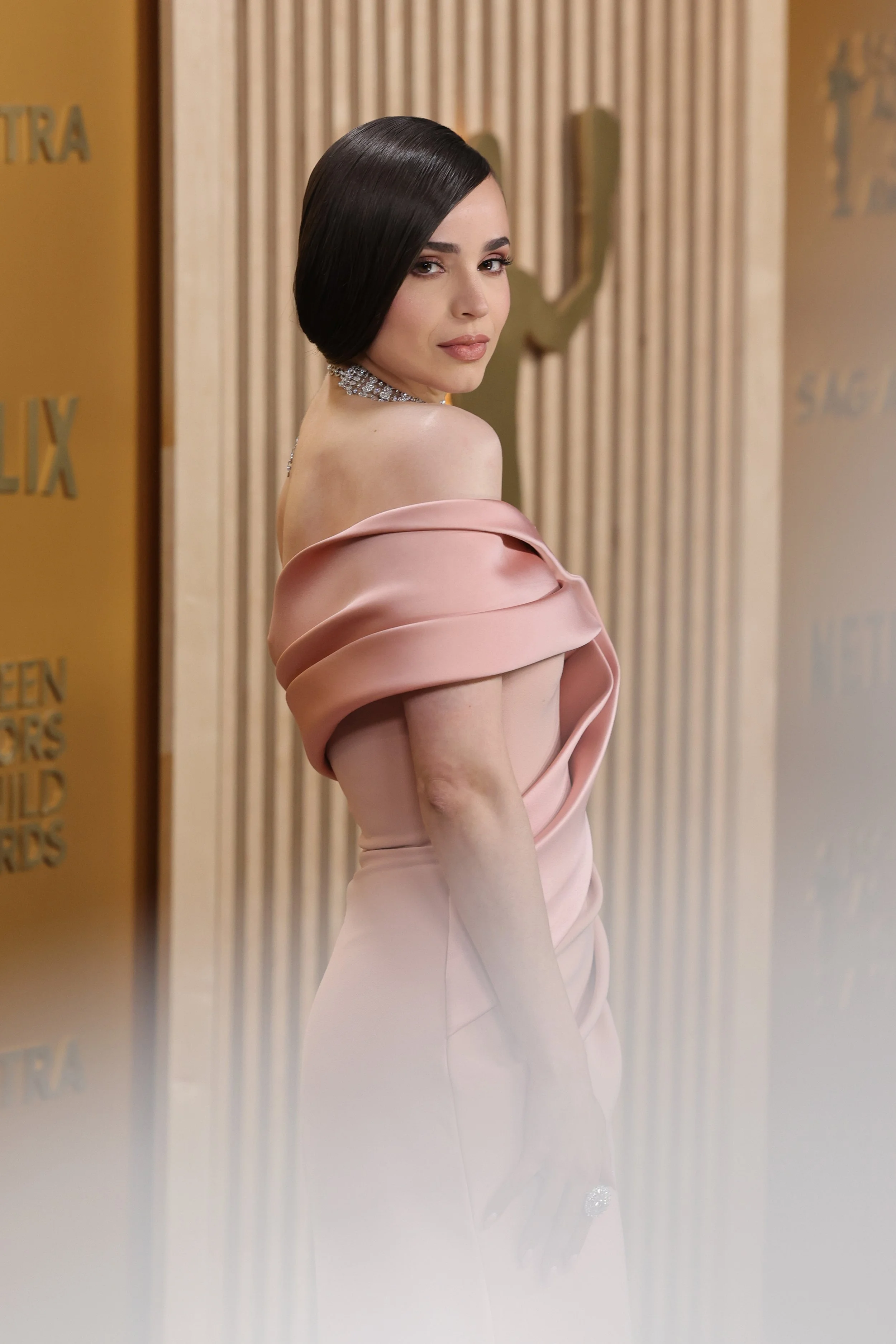 A woman in a pink off-shoulder gown looking over her shoulder at a red carpet event.