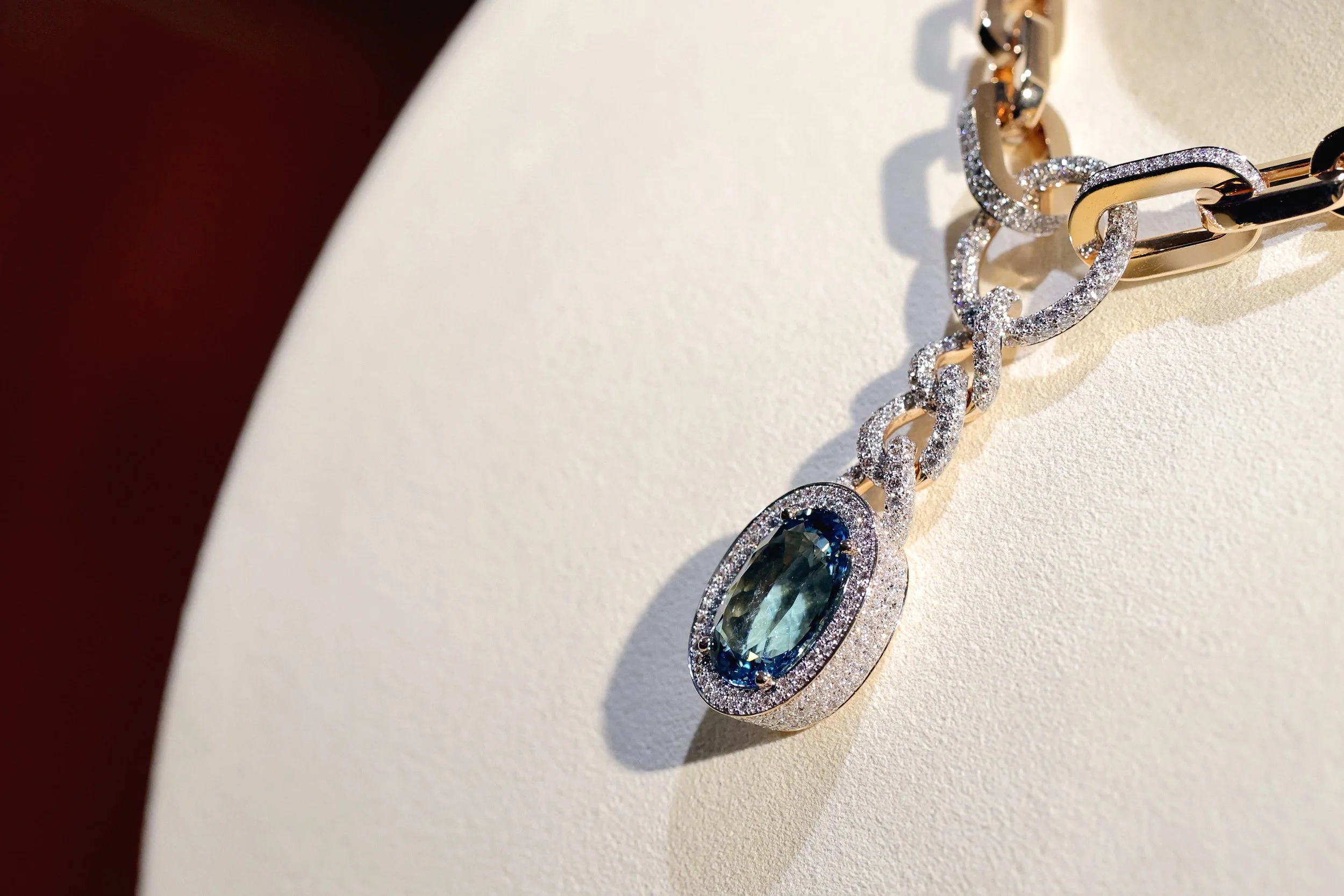 Close-up of a gold and silver chain necklace with a large oval-shaped blue gemstone pendant surrounded by small diamonds.