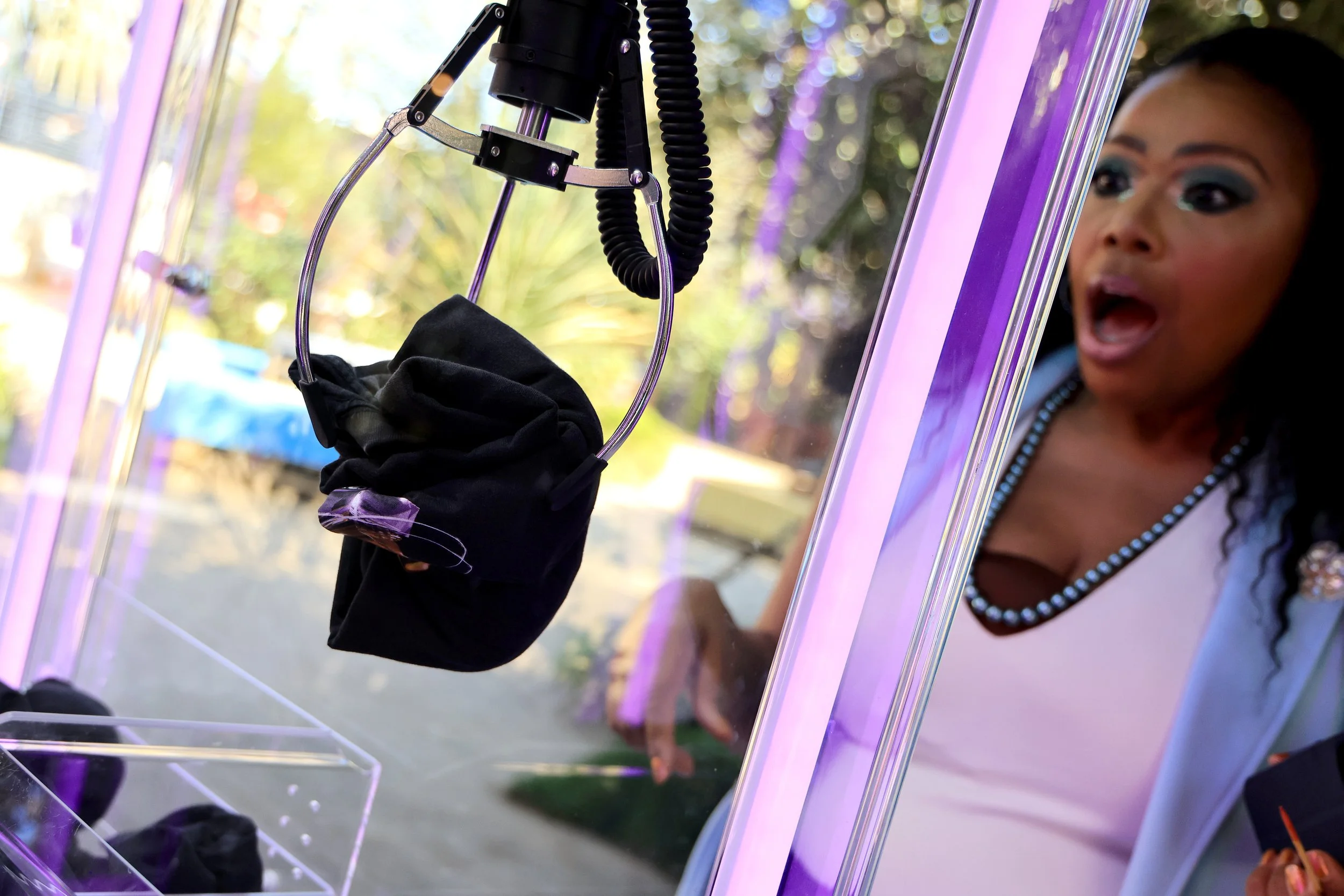 Woman with surprised expression looking at a claw machine with a black face mask inside.