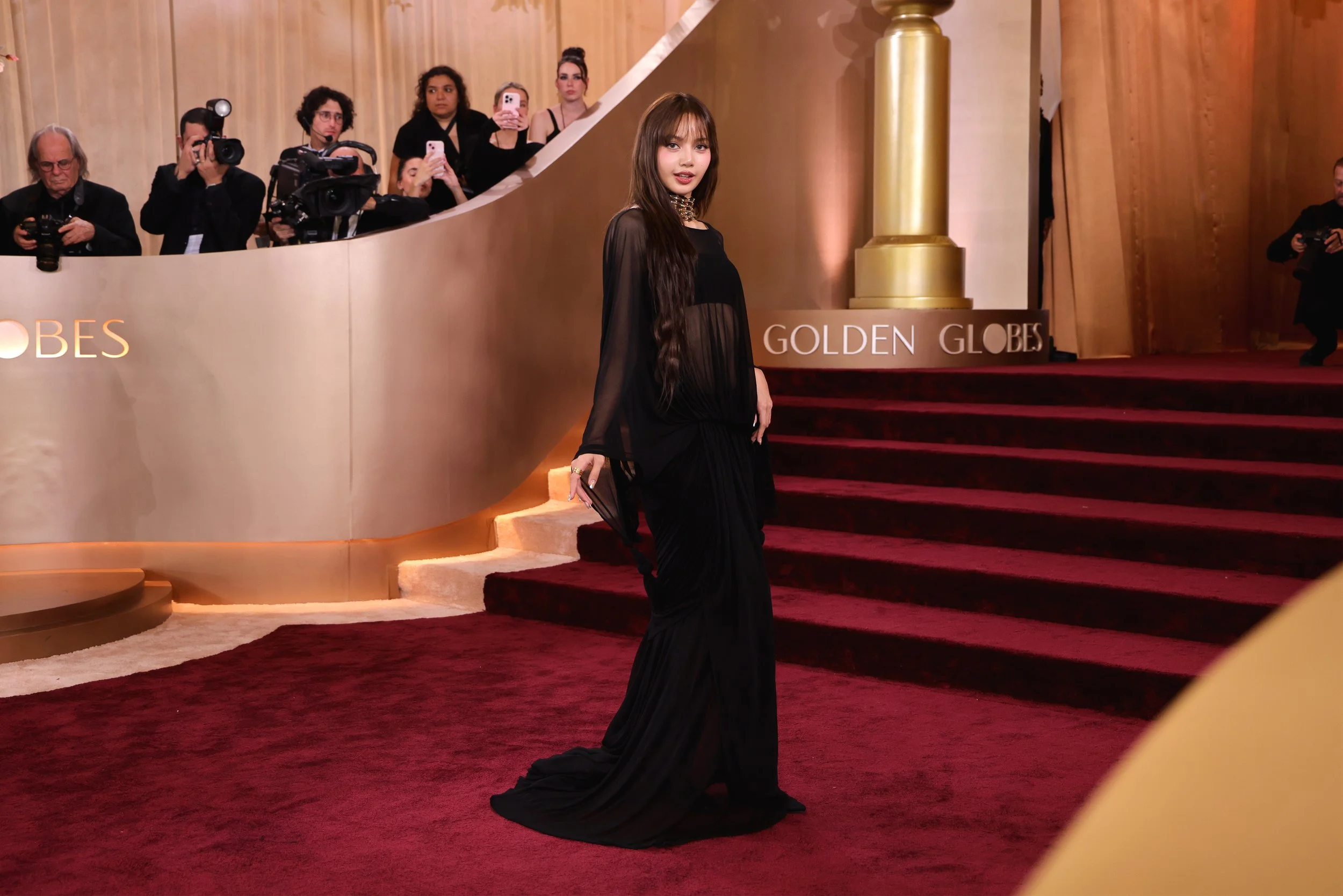 A woman in a black gown standing on a red carpet at an awards event, with photographers and spectators taking pictures in the background.