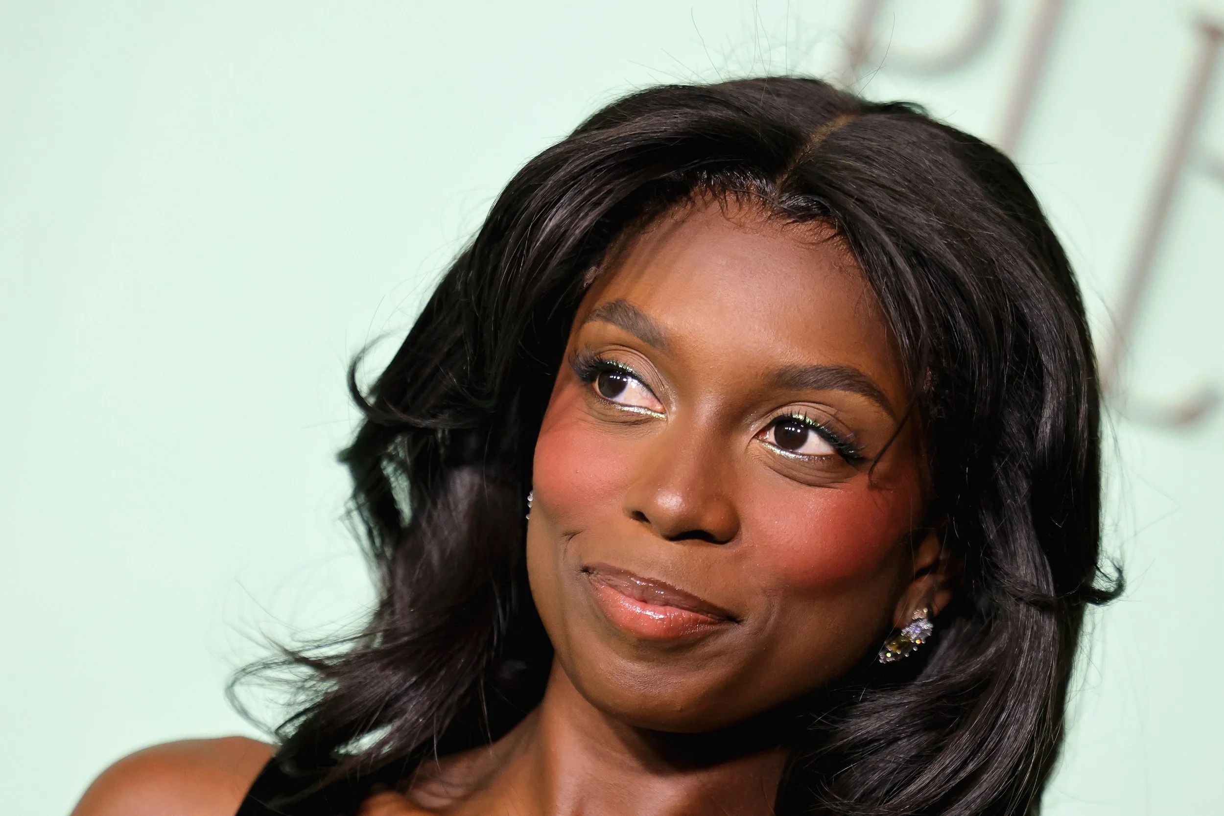 Close-up of an African American woman with medium-length black hair, wearing makeup and earrings, looking to the side with a soft smile.
