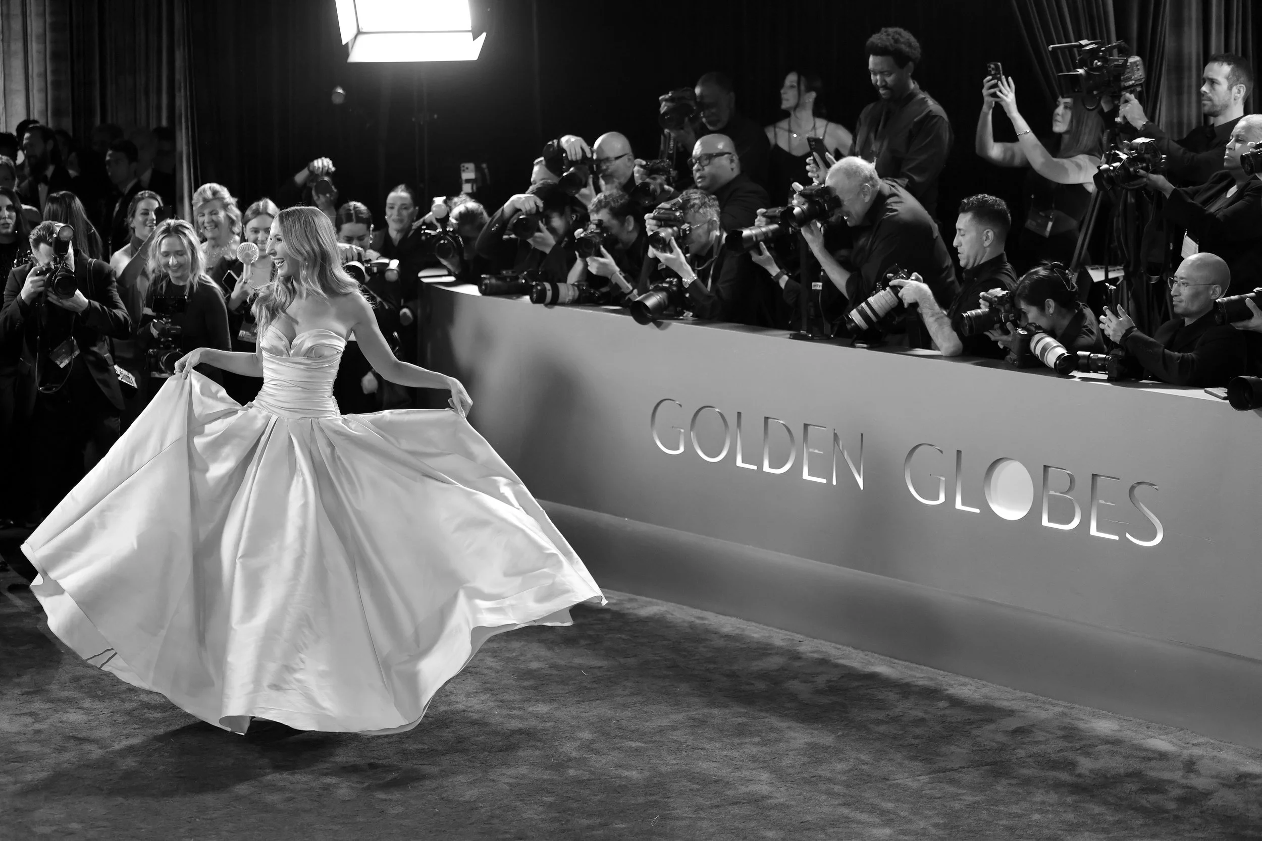 A woman in an elegant gown twirls on the red carpet at the Golden Globes, surrounded by photographers and attendees.