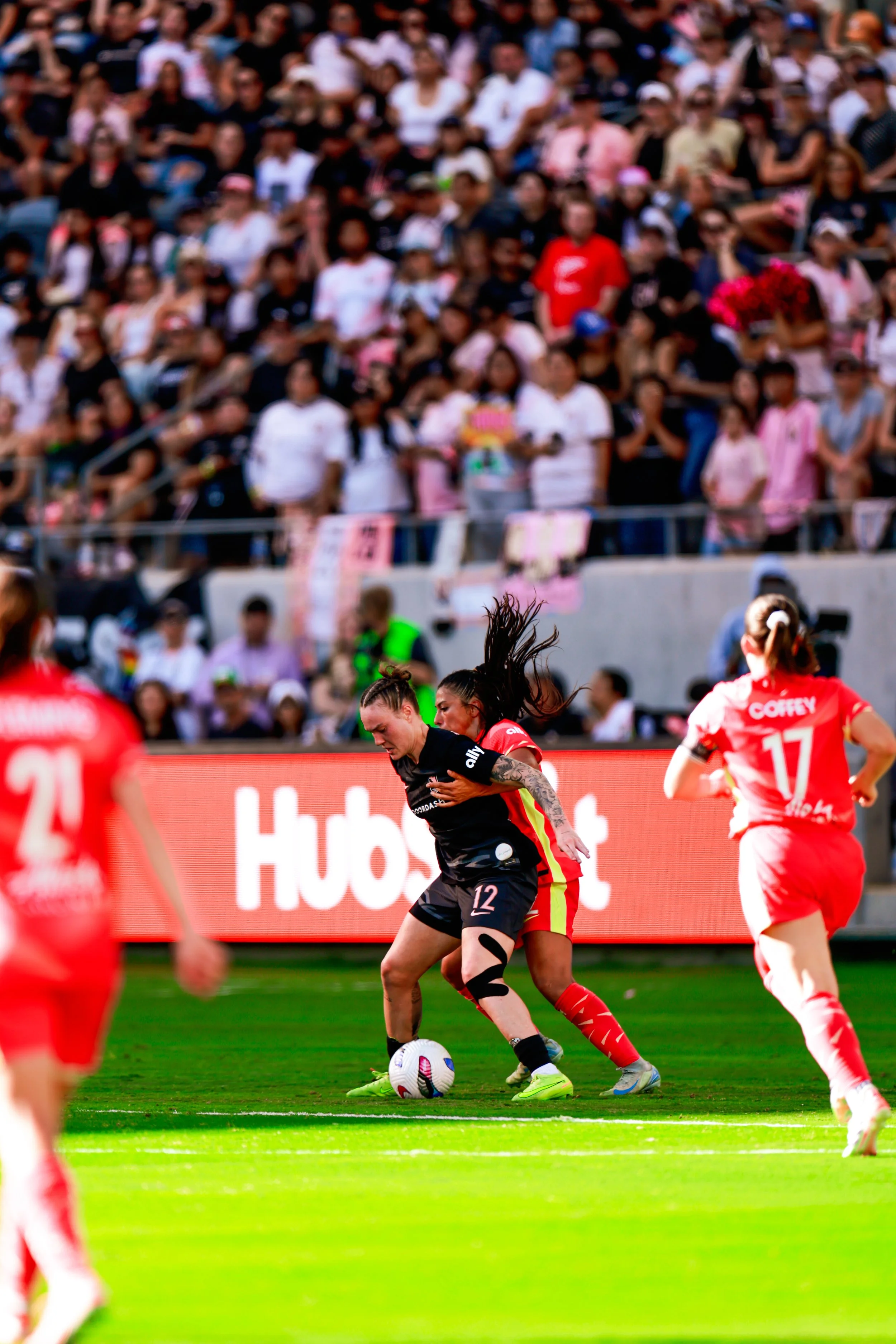 Women soccer players competing for the ball on a green field with spectators in the stands.