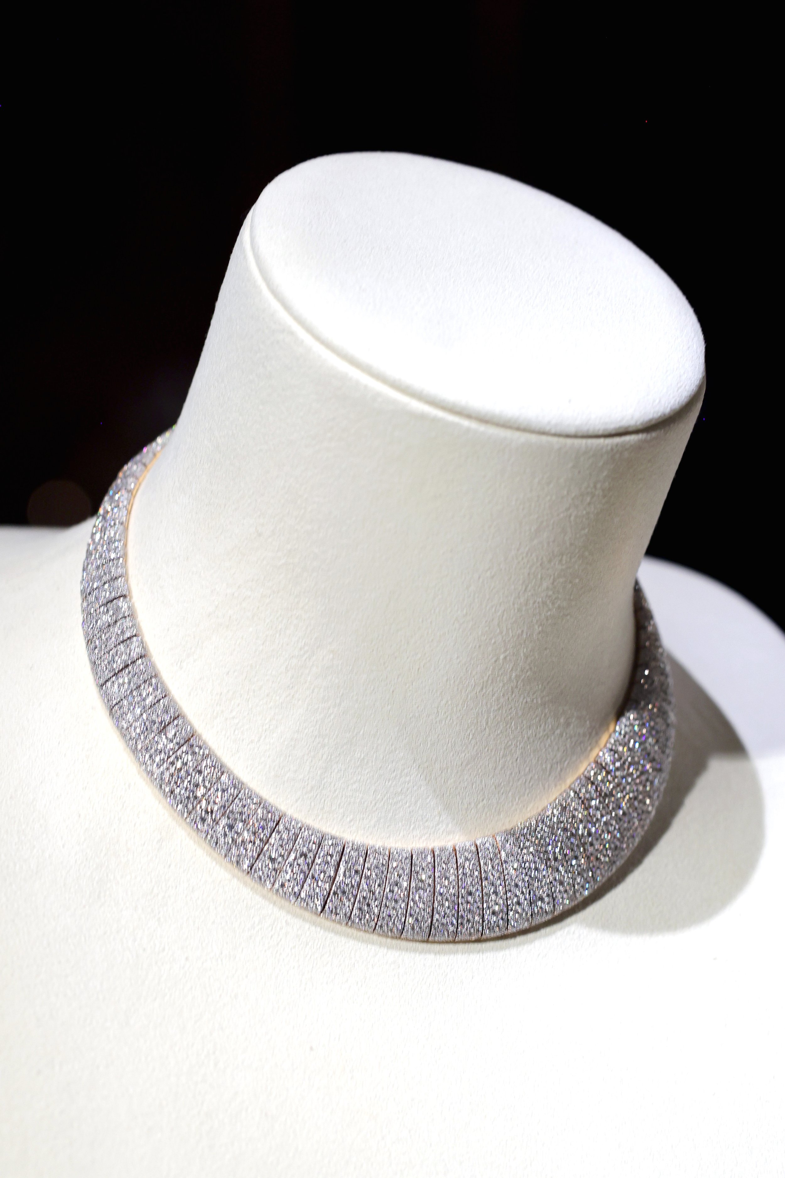 A diamond necklace displayed on a white jewelry bust with a black background.