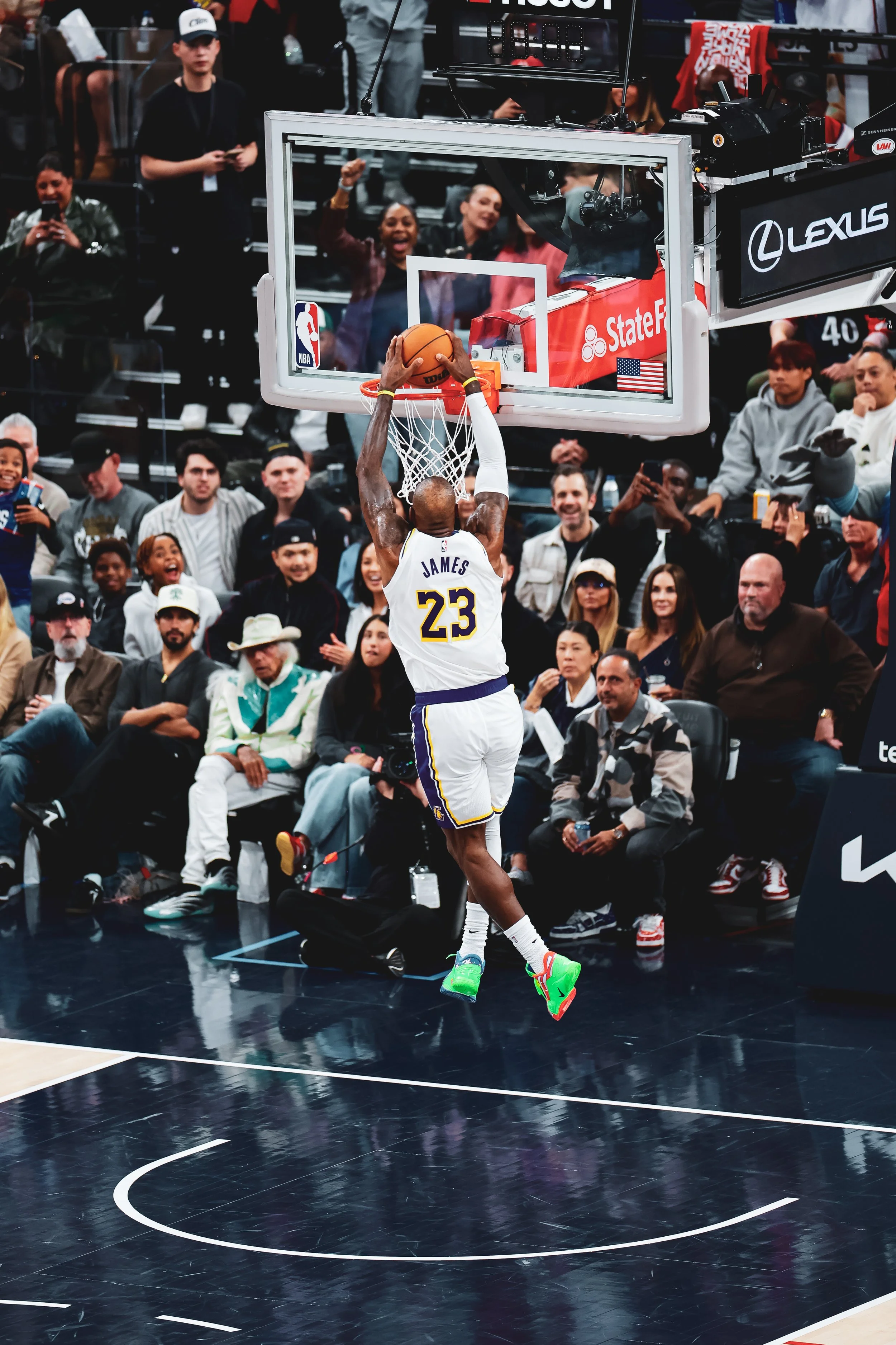 A basketball player wearing a number 23 jersey with the name James is mid-air dunking the ball into the hoop during a game, with spectators watching and cheering in the background.