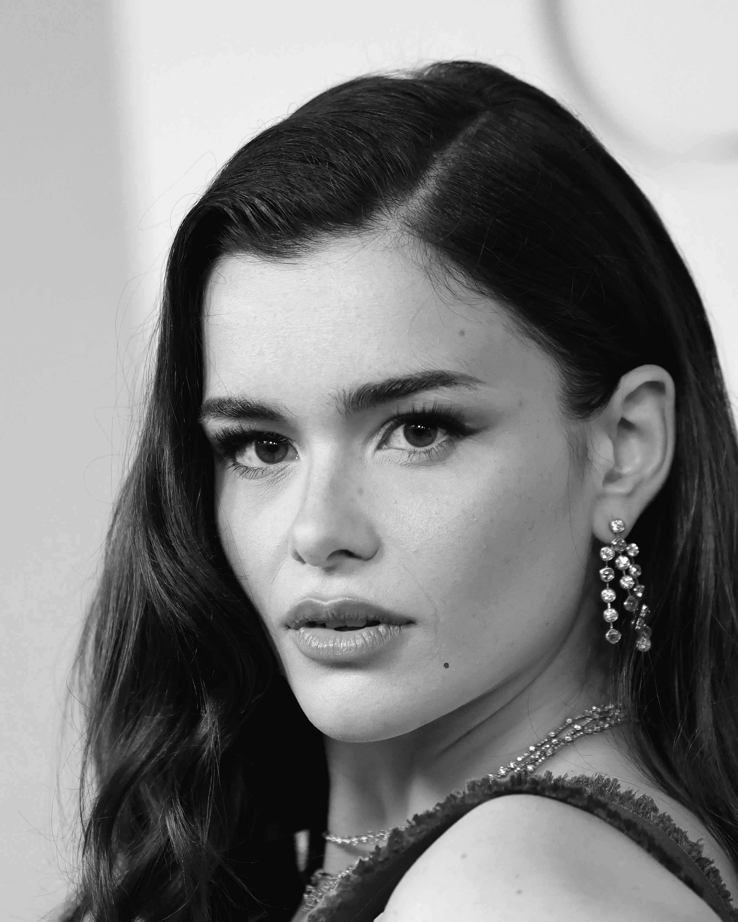 Black and white close-up portrait of a woman with dark hair, wearing earrings, and a necklace, looking at the camera with a serious expression.