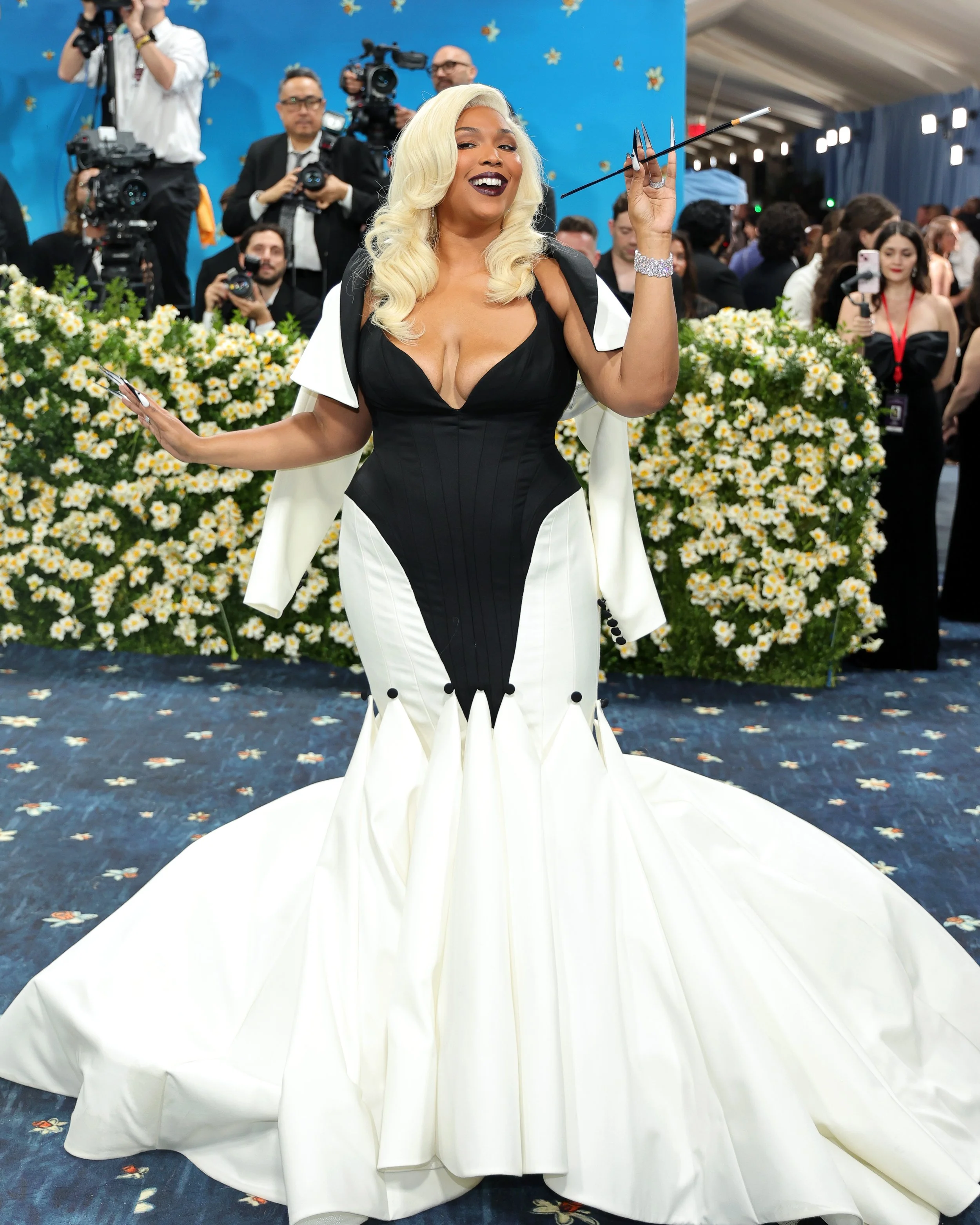 Woman with platinum blonde hair in a black and white gown at a formal event with cameras and photographers in the background.