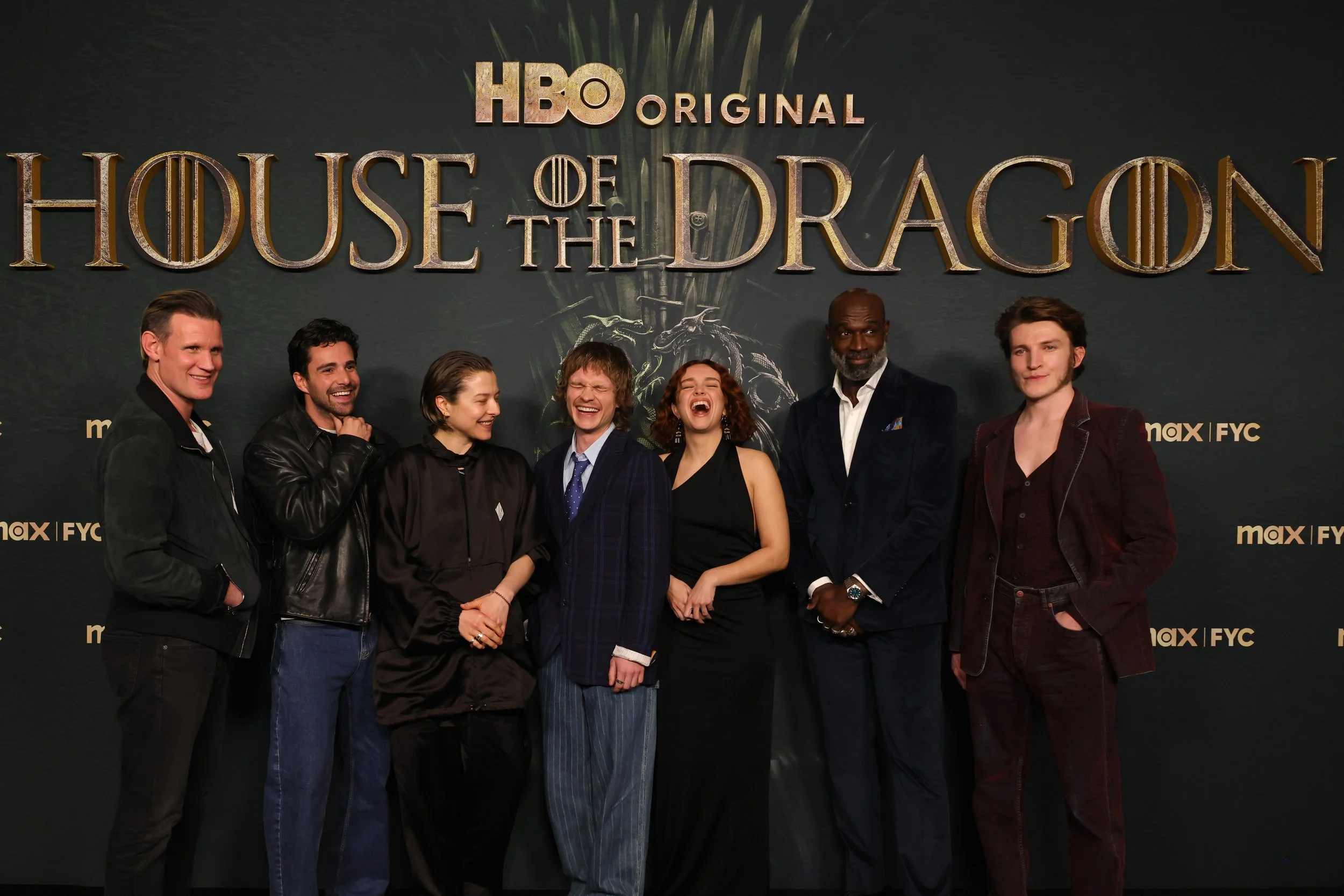 Group of seven actors standing in front of a "House of the Dragon" HBO promotional backdrop, smiling and posing for a photo.