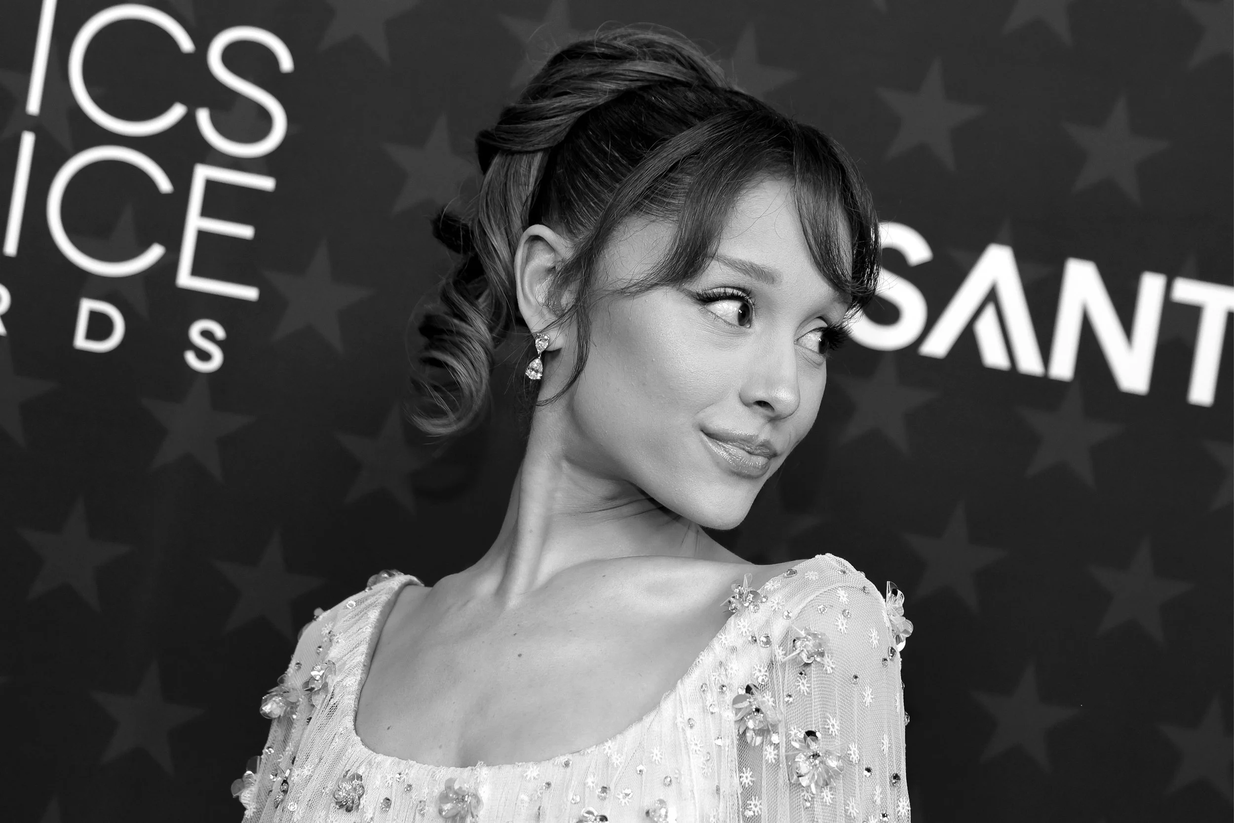 A woman with styled hair and jewelry smiling and looking to her right in front of a backdrop with stars and the words 'SANT' and part of 'POLITICS'.