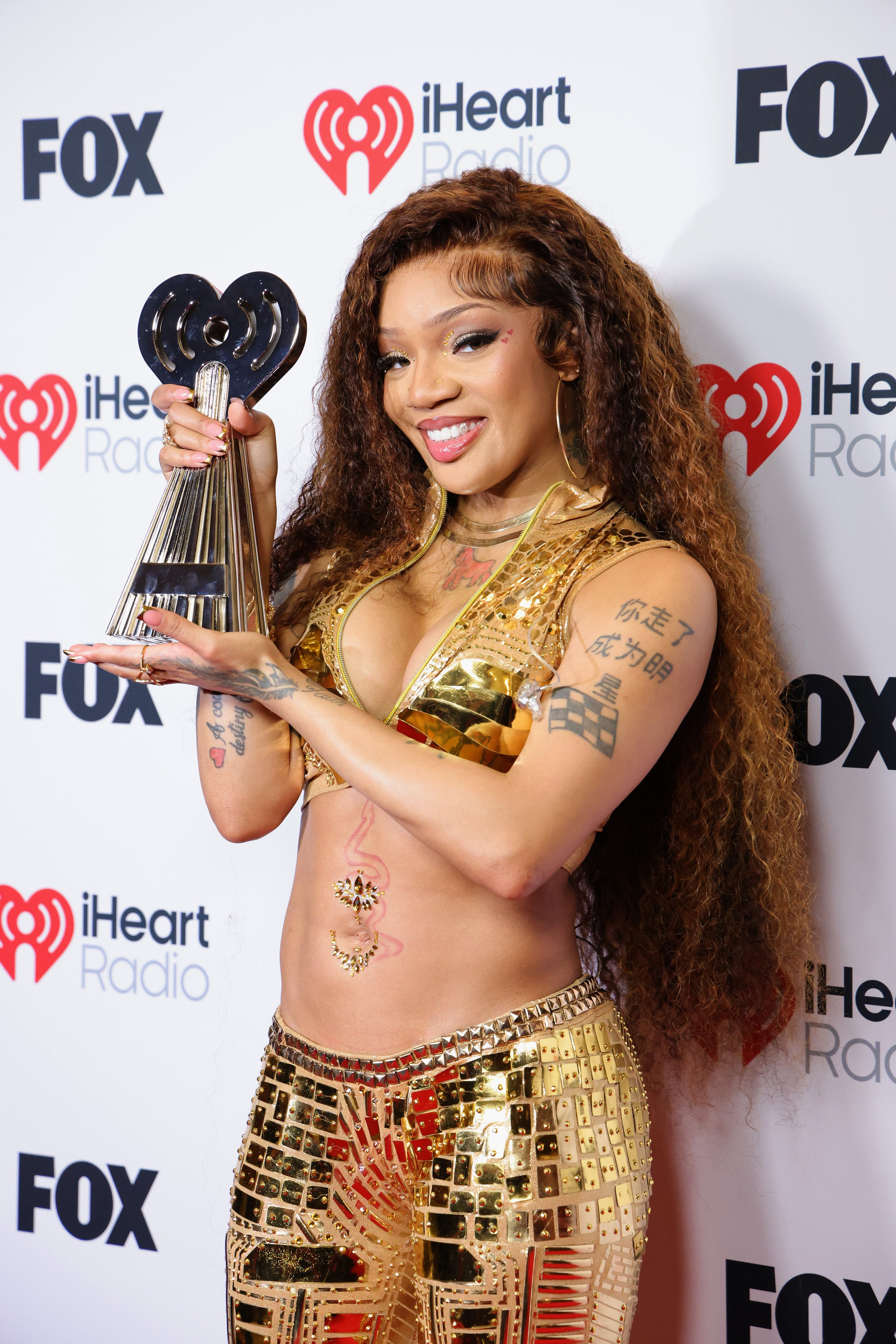 Woman with long curly hair in a gold outfit holding a iHeartRadio award