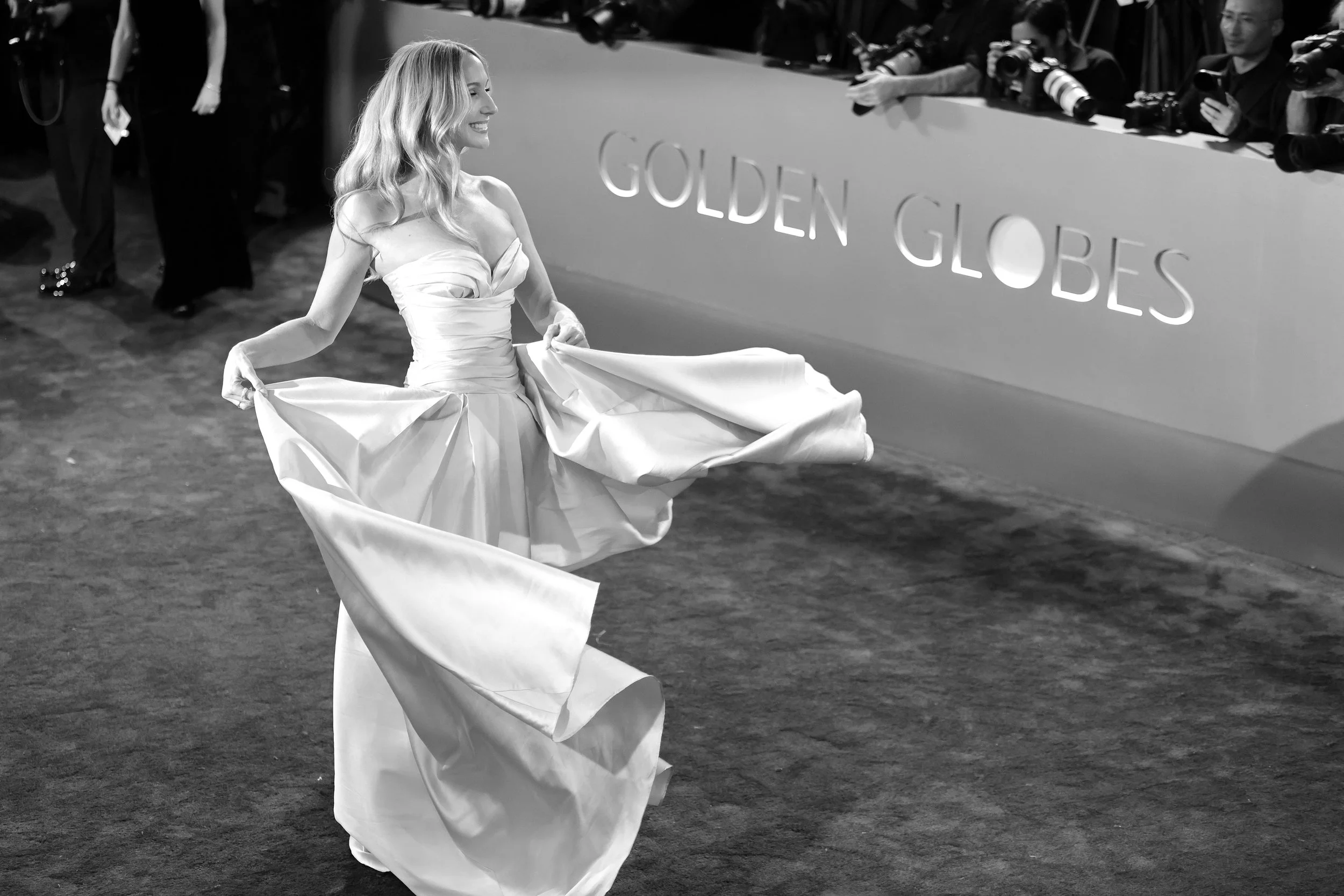 A woman in a strapless, ballgown-style dress twirling on the red carpet at the Golden Globes awards show, with photographers taking pictures in the background.