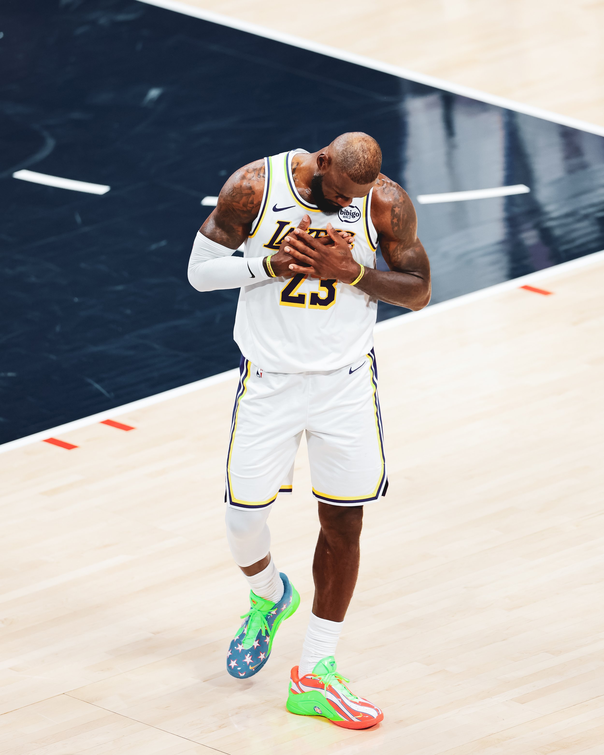 LeBron James, wearing a Los Angeles Lakers jersey with the number 23, standing on a basketball court with his hand over his chest, wearing colorful basketball shoes.