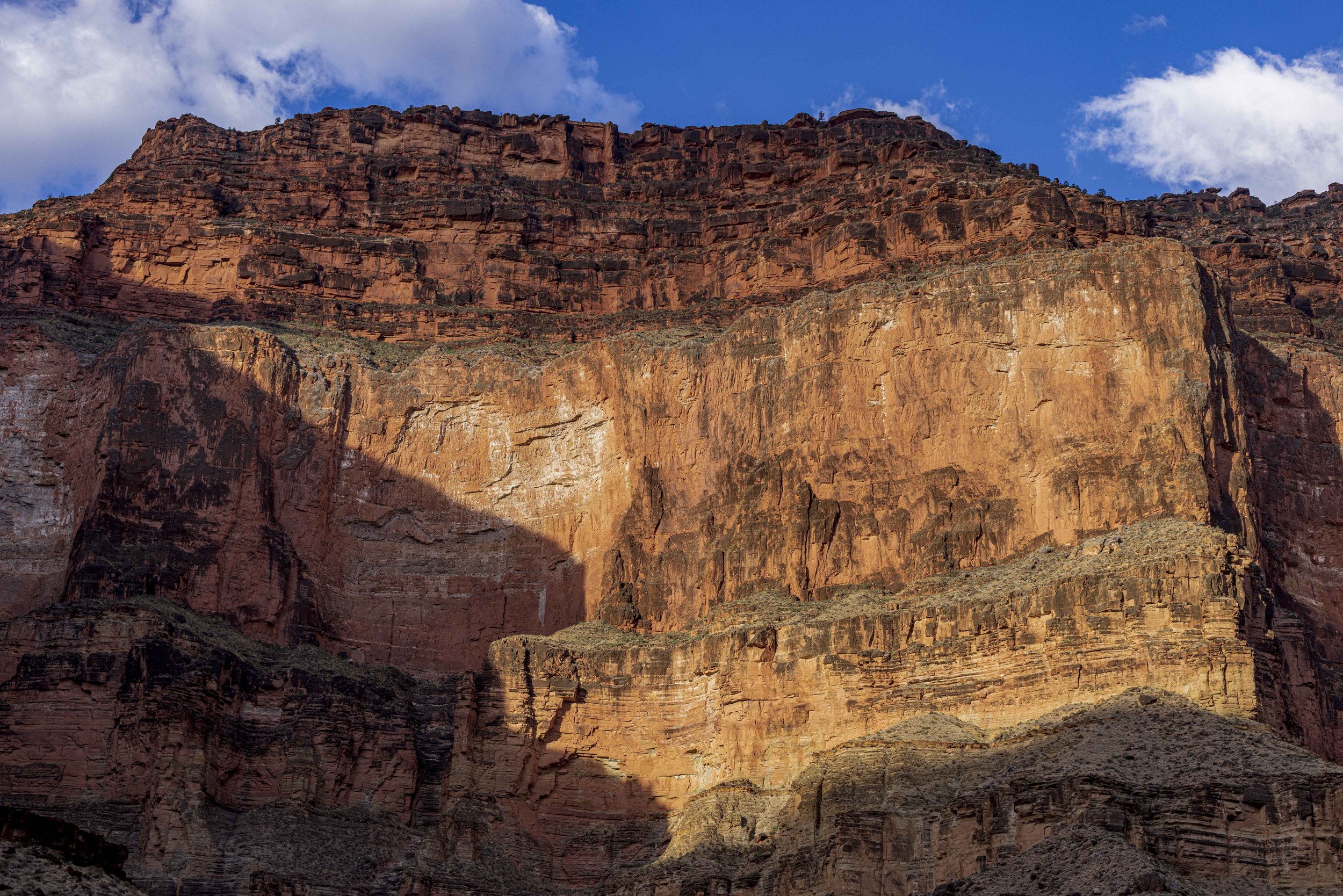Close-up of the red and orange rocky cliffs of the Grand Canyon with a partly cloudy blue sky.