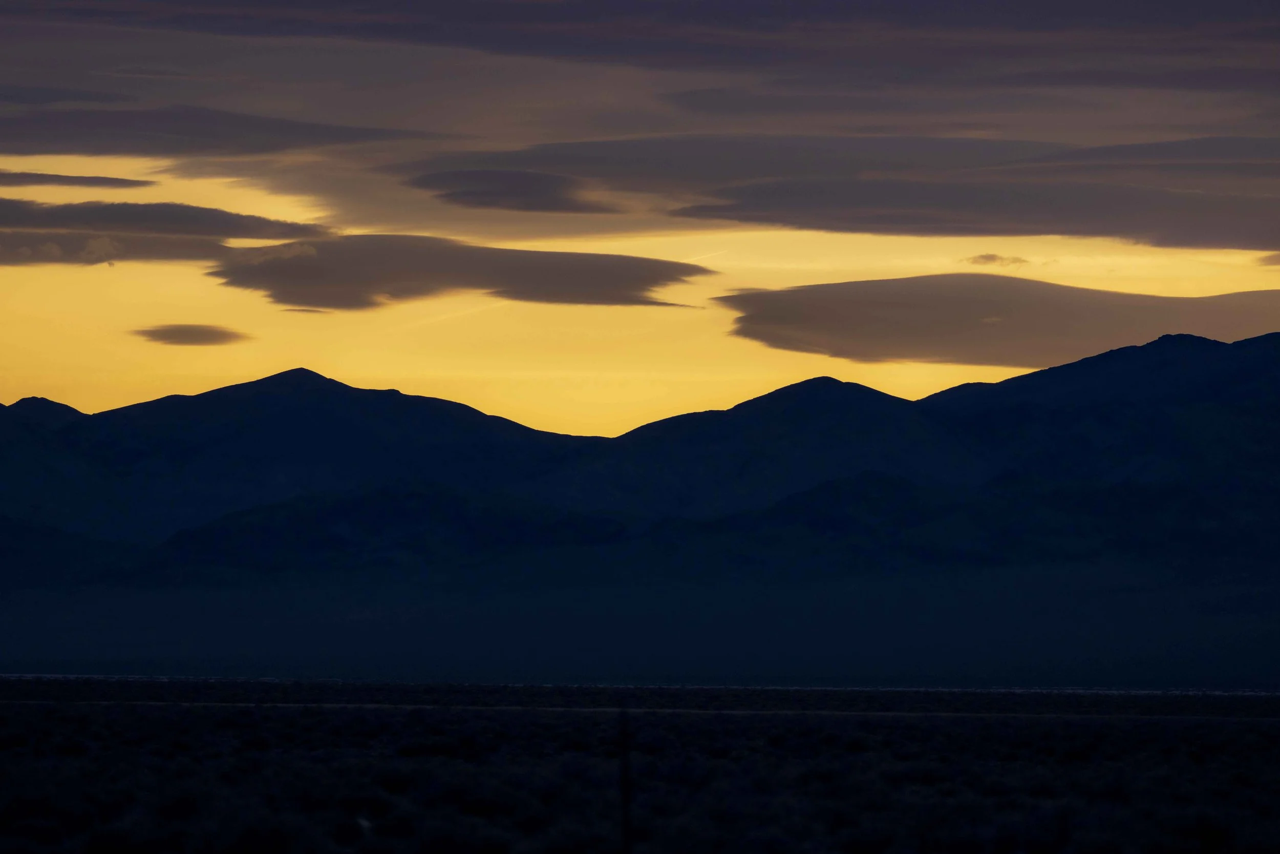 Silhouette of mountain range during sunset with dark clouds in the sky.