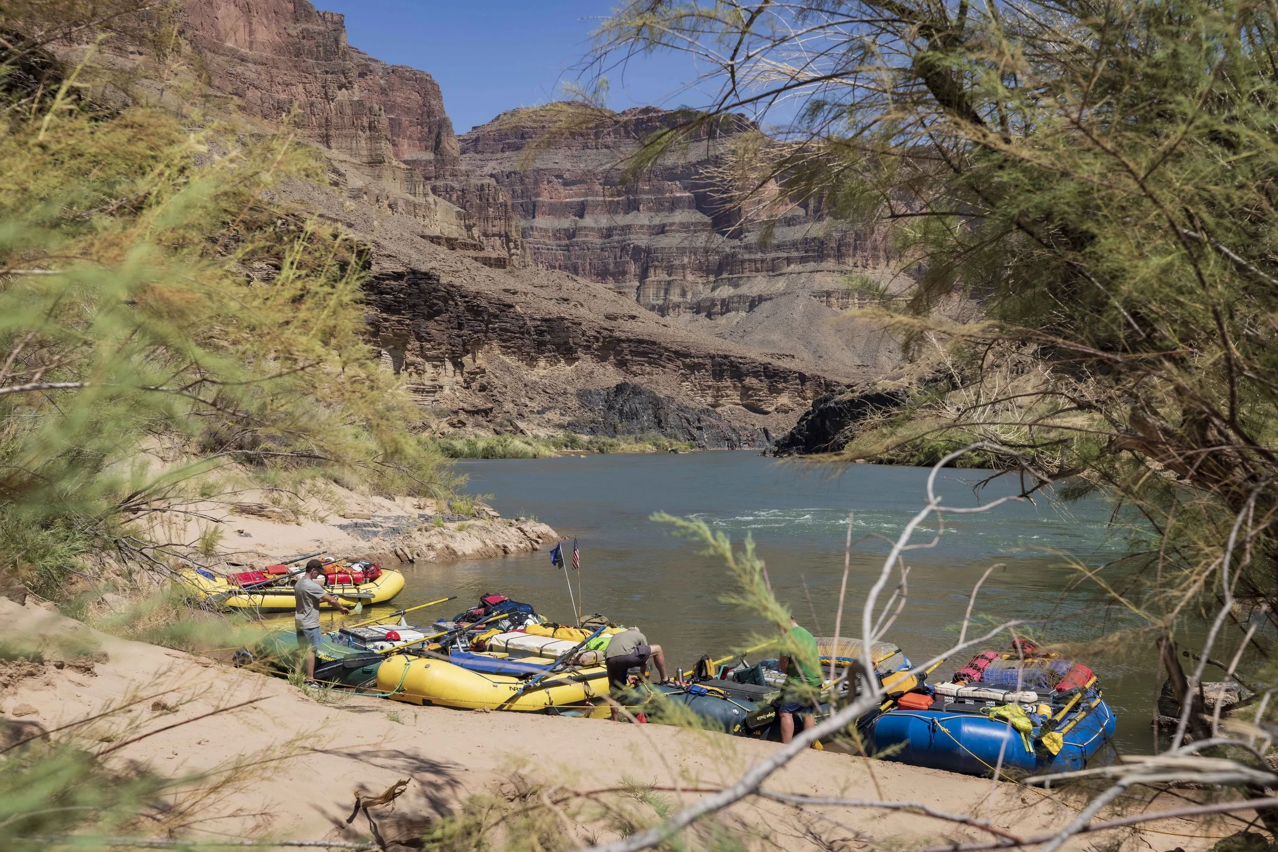 People preparing inflatable rafts for a river trip in the Grand Canyon with canyon walls and blue sky in the background.
