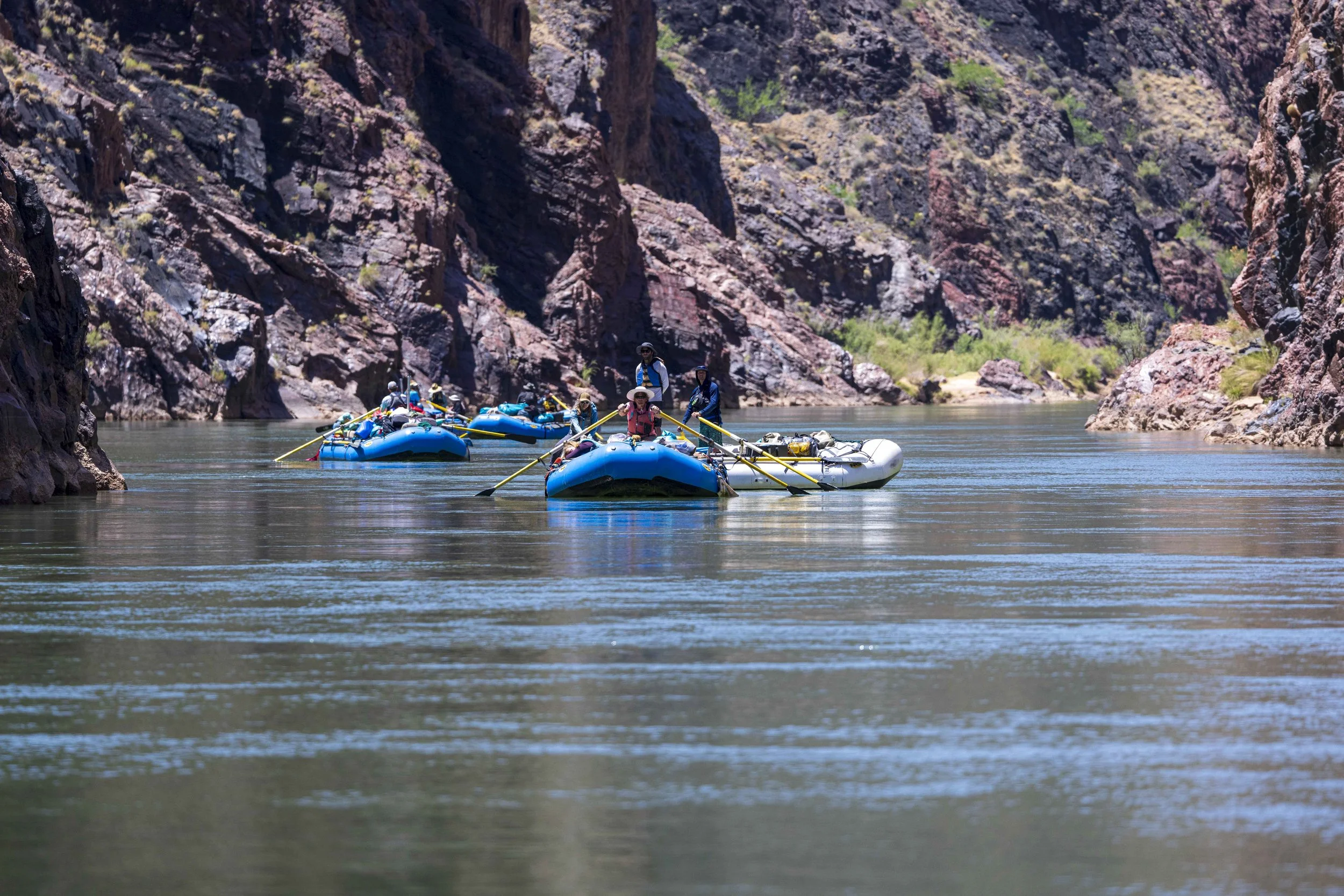 A group of people rafting on a calm river surrounded by tall, rocky canyon walls.