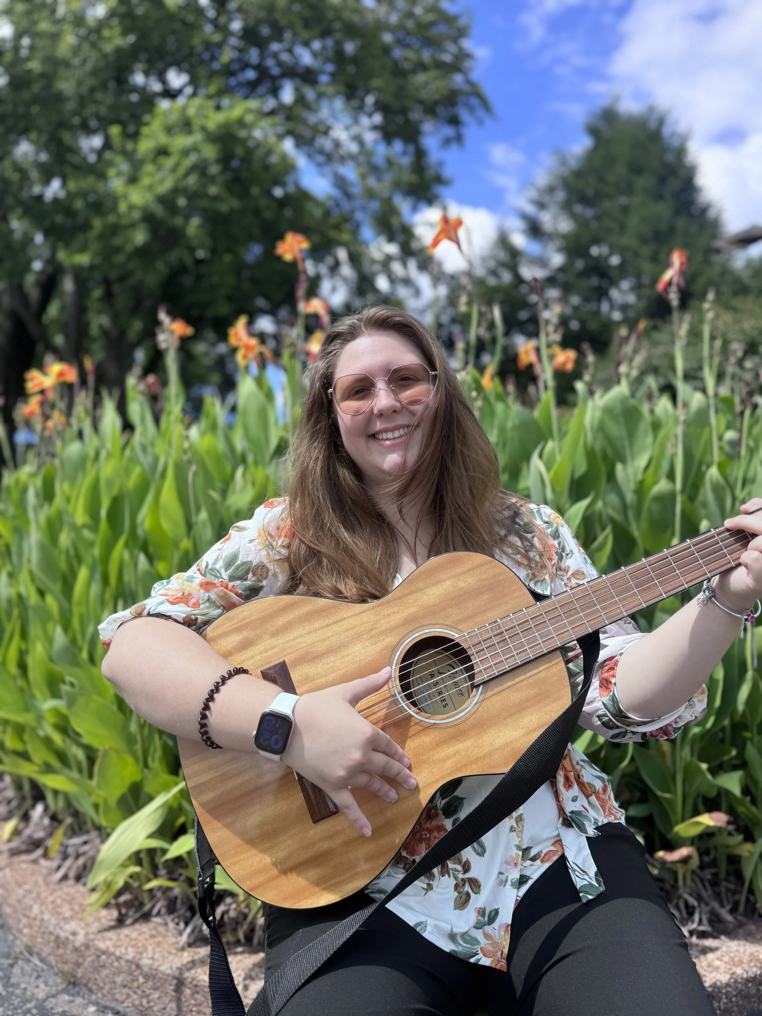 Young girl with a flower shirt holding a guitar smiling