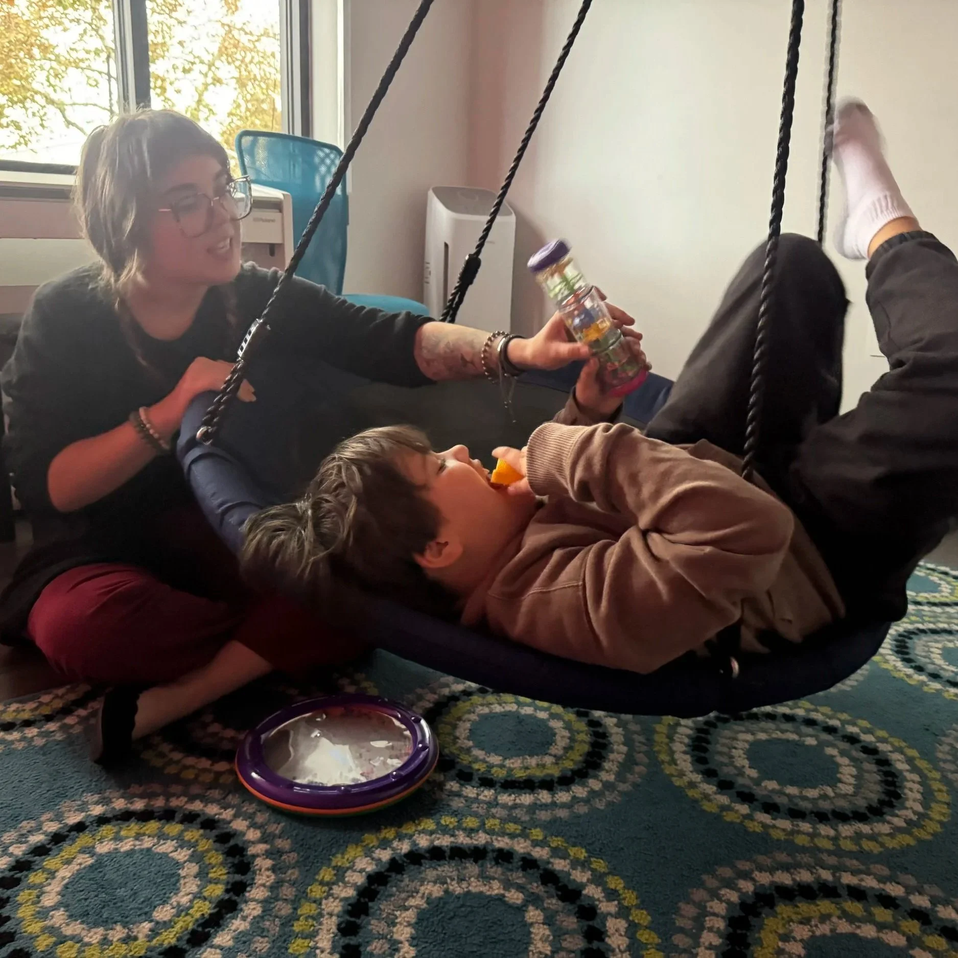 Young boy swinging in the dark with a rainstick and his female therapist