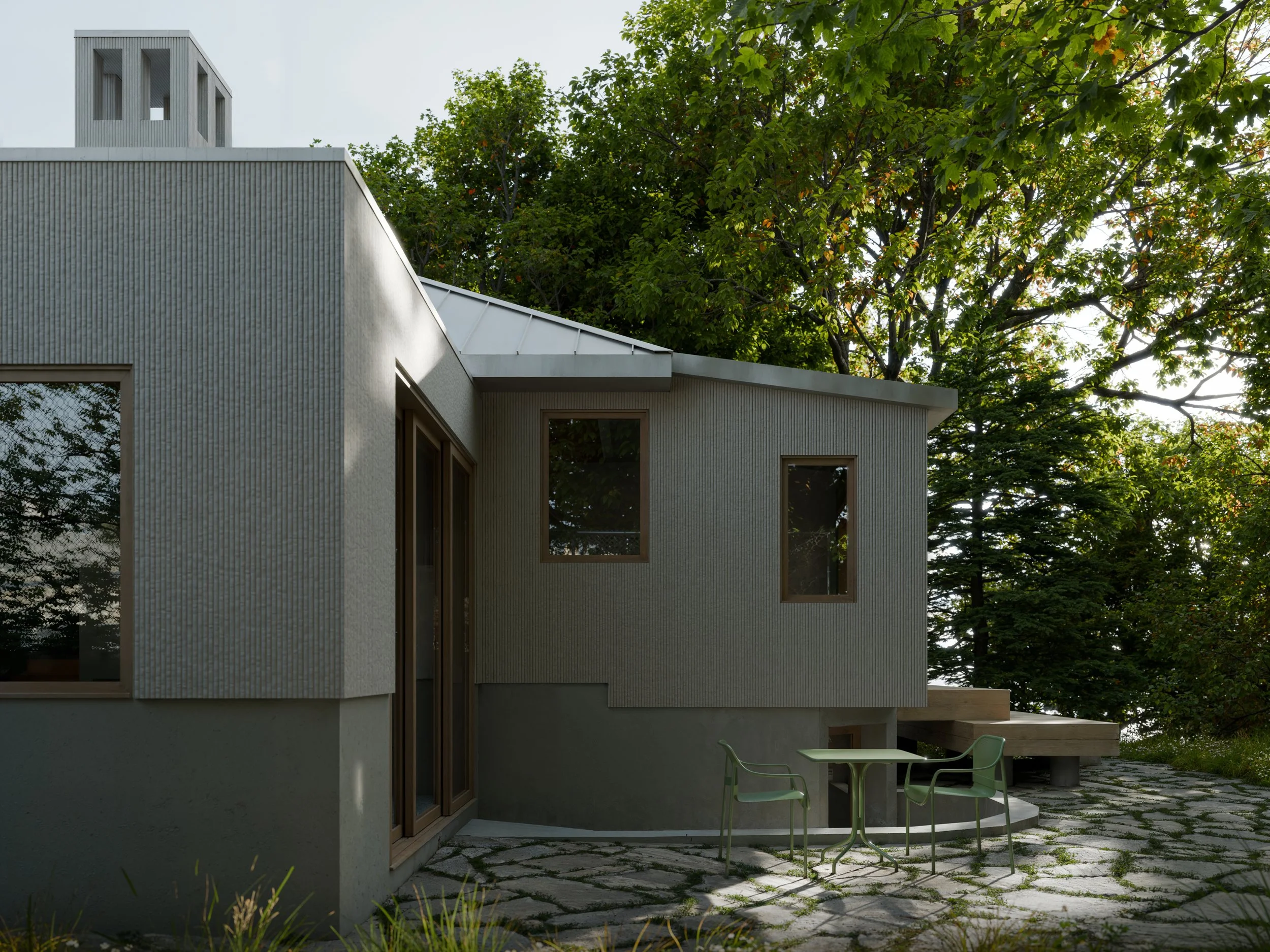 Modern house with gray exterior walls, large windows, outdoor patio with green table and chairs, and surrounded by trees.