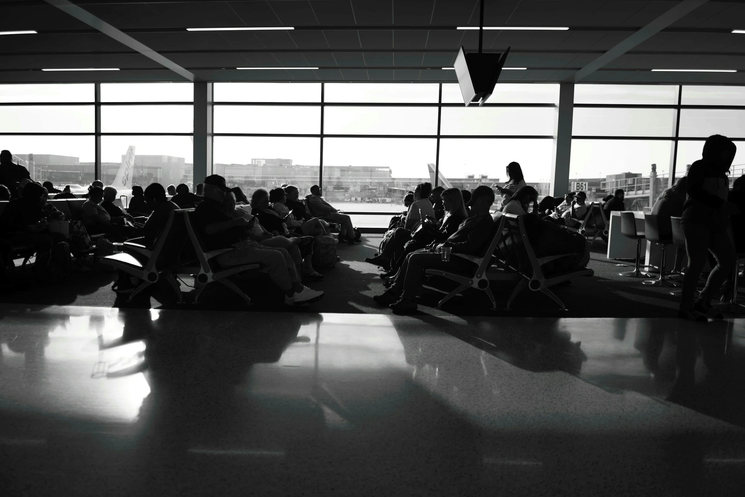 Travelers waiting at an airport departure gate after a flight cancellation while checking updated flight information.