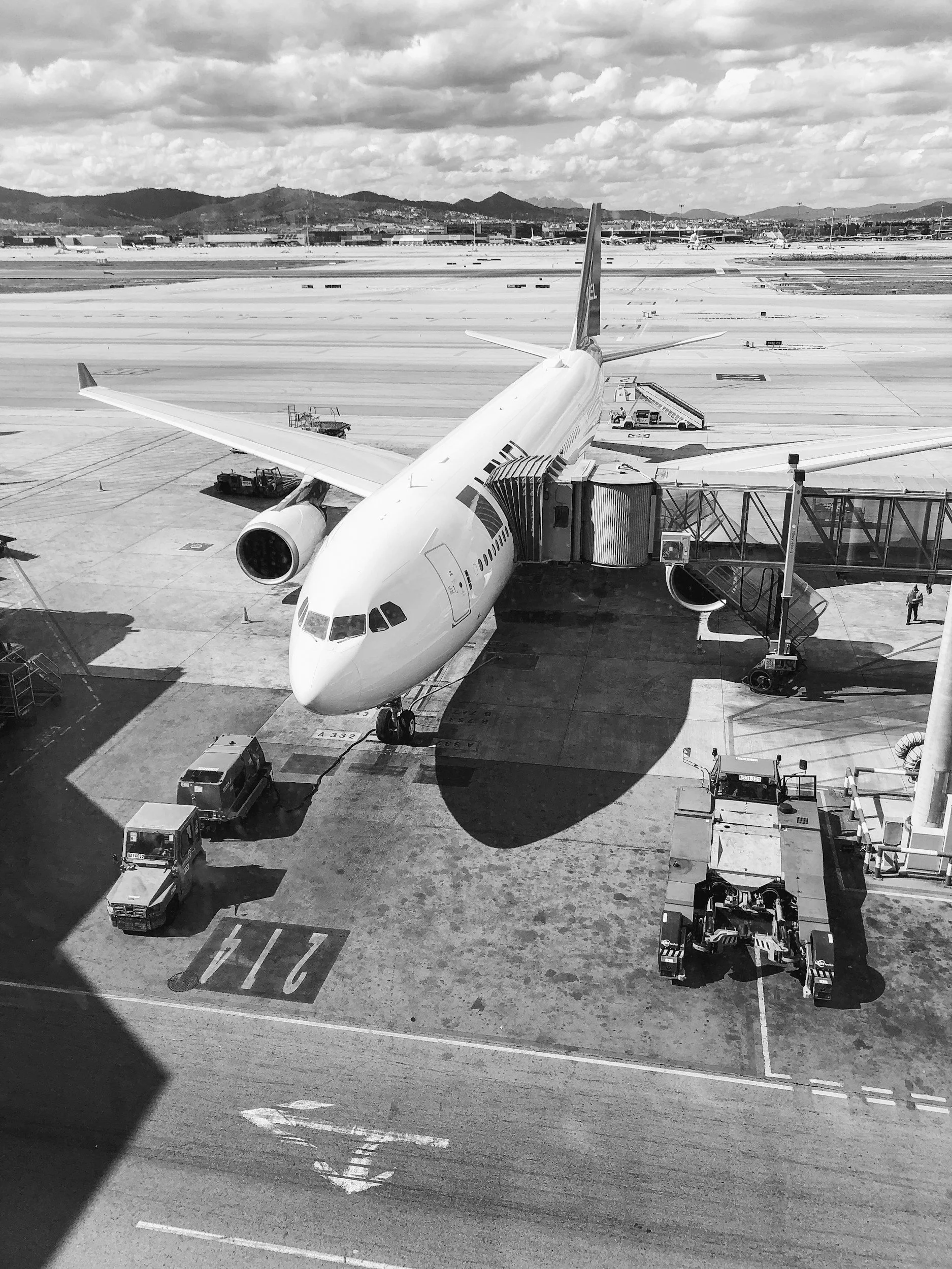 Black and white photograph of a commercial airplane parked at an airport gate before departure.