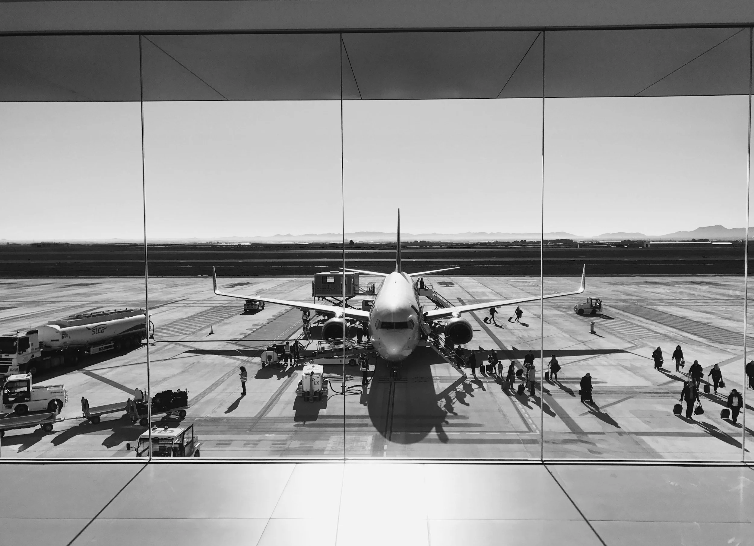 Black and white photo of passengers boarding a commercial airplane viewed from inside an airport terminal.