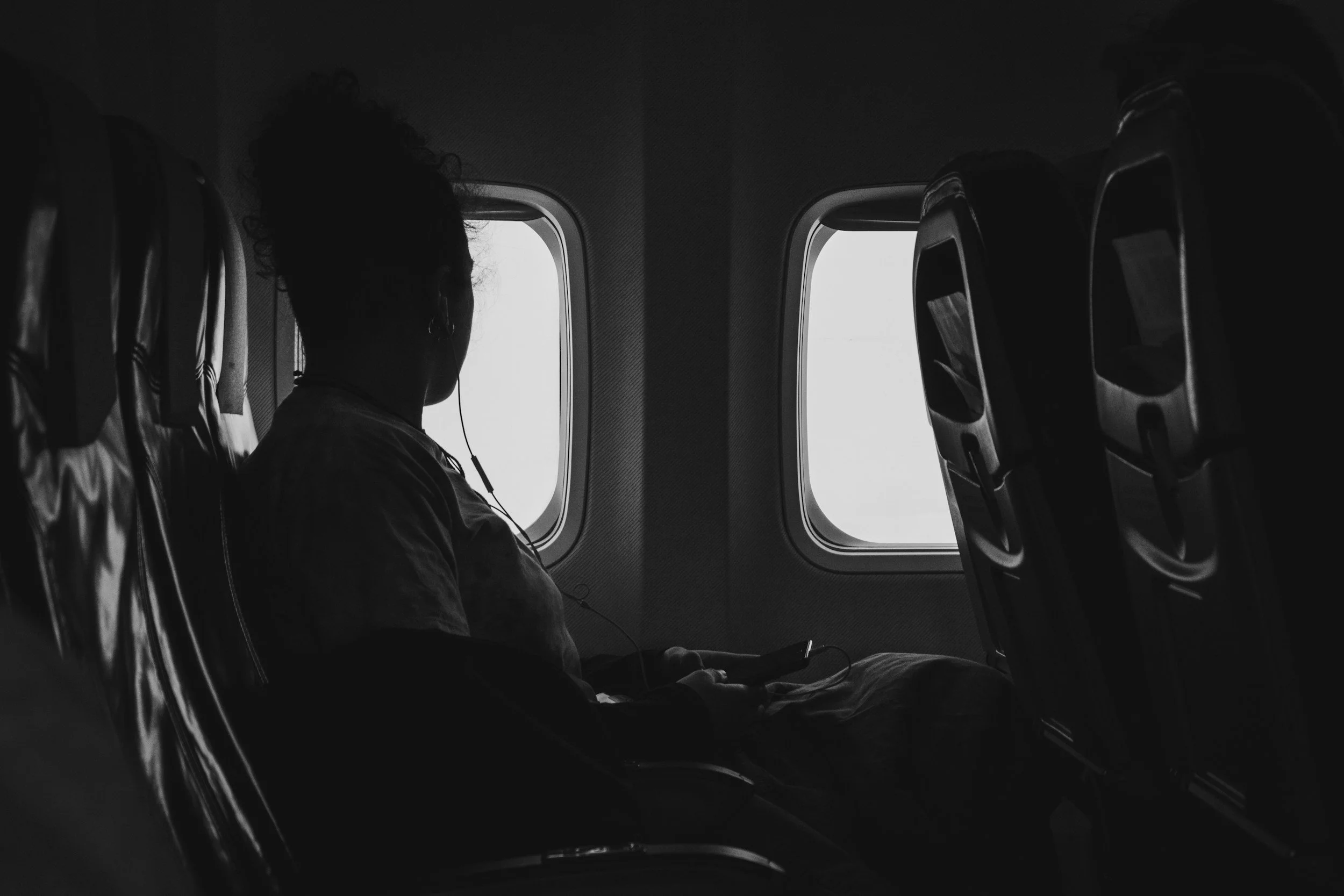 A traveler seated on an airplane looking out the window, waiting for their flight to depart.