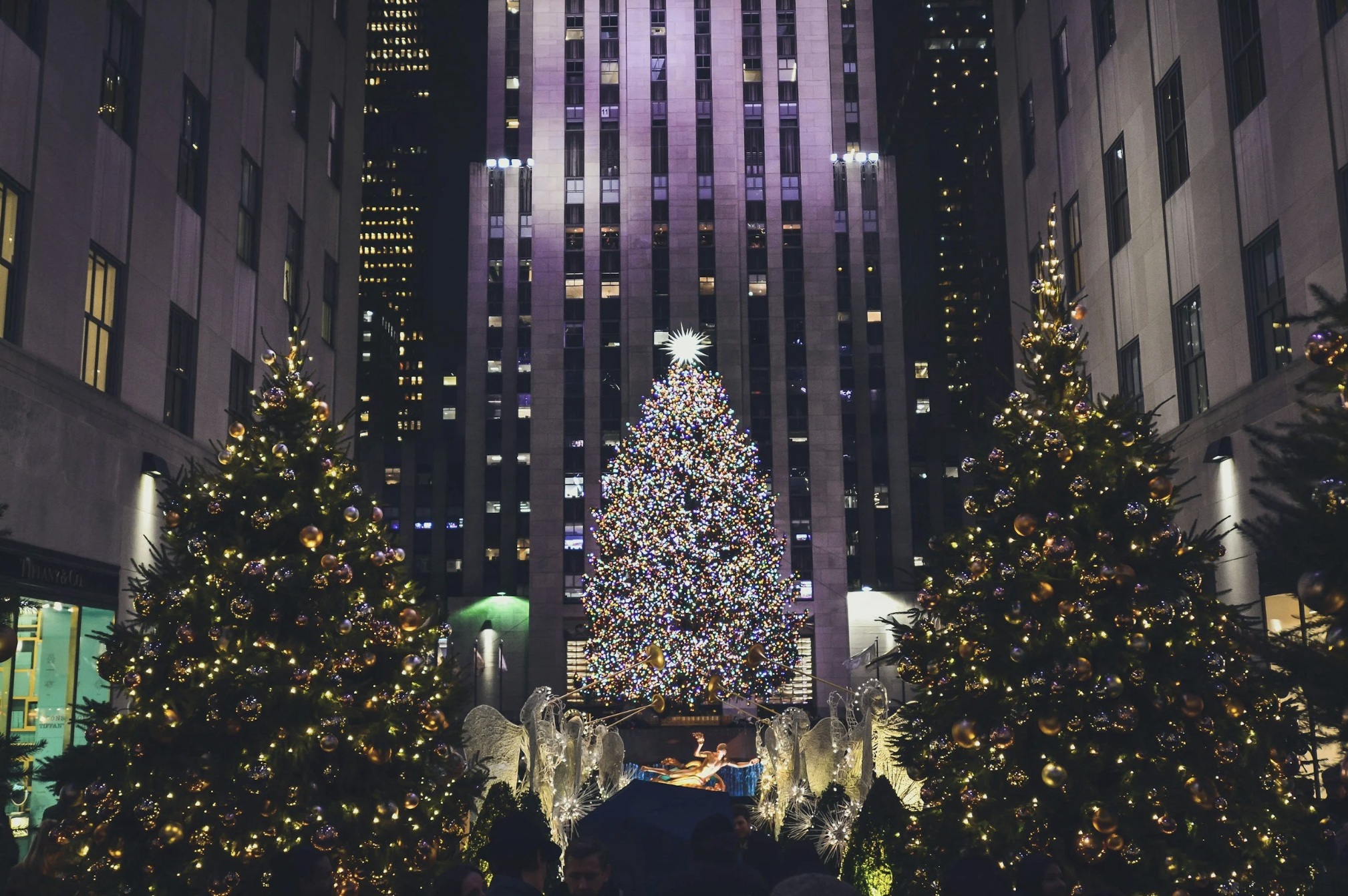 Rockefeller Center Christmas Tree illuminated with colorful lights and surrounded by decorated Christmas trees in New York City during the holiday season.