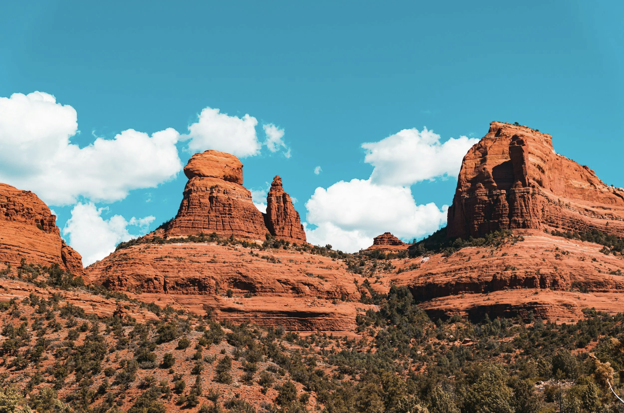 Red rock formations in Sedona, Arizona, beneath a bright blue sky with white clouds.