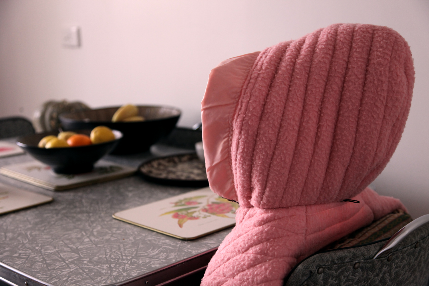Hooded pink jacket sitting alone at kitchen table.