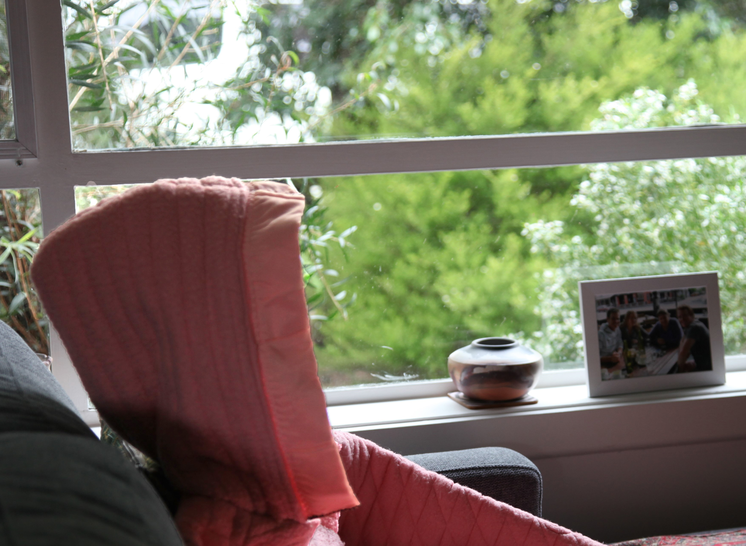 Hooded pink jacket sitting alone on couch next to a window.