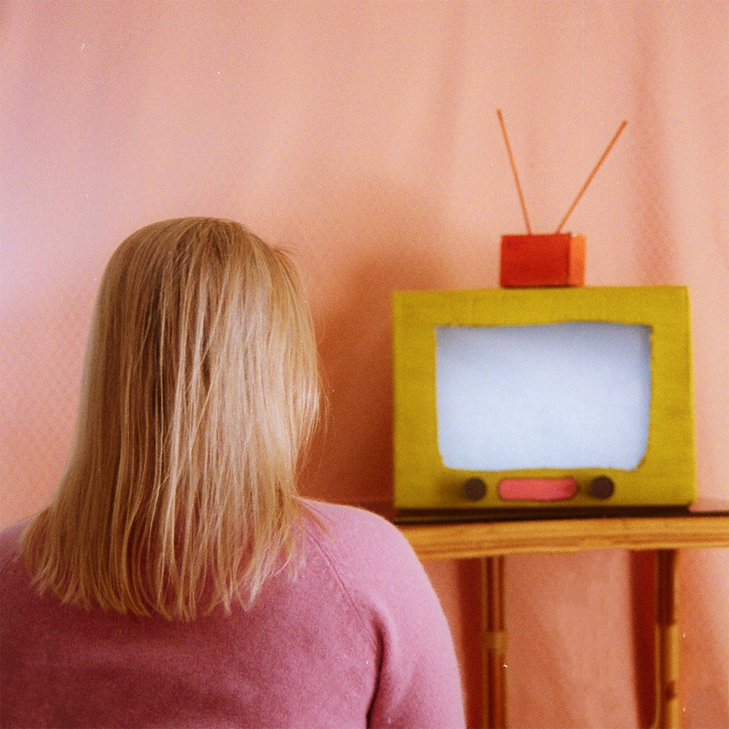 Colour photograph depicting girl sitting in front of static cardboard TV.