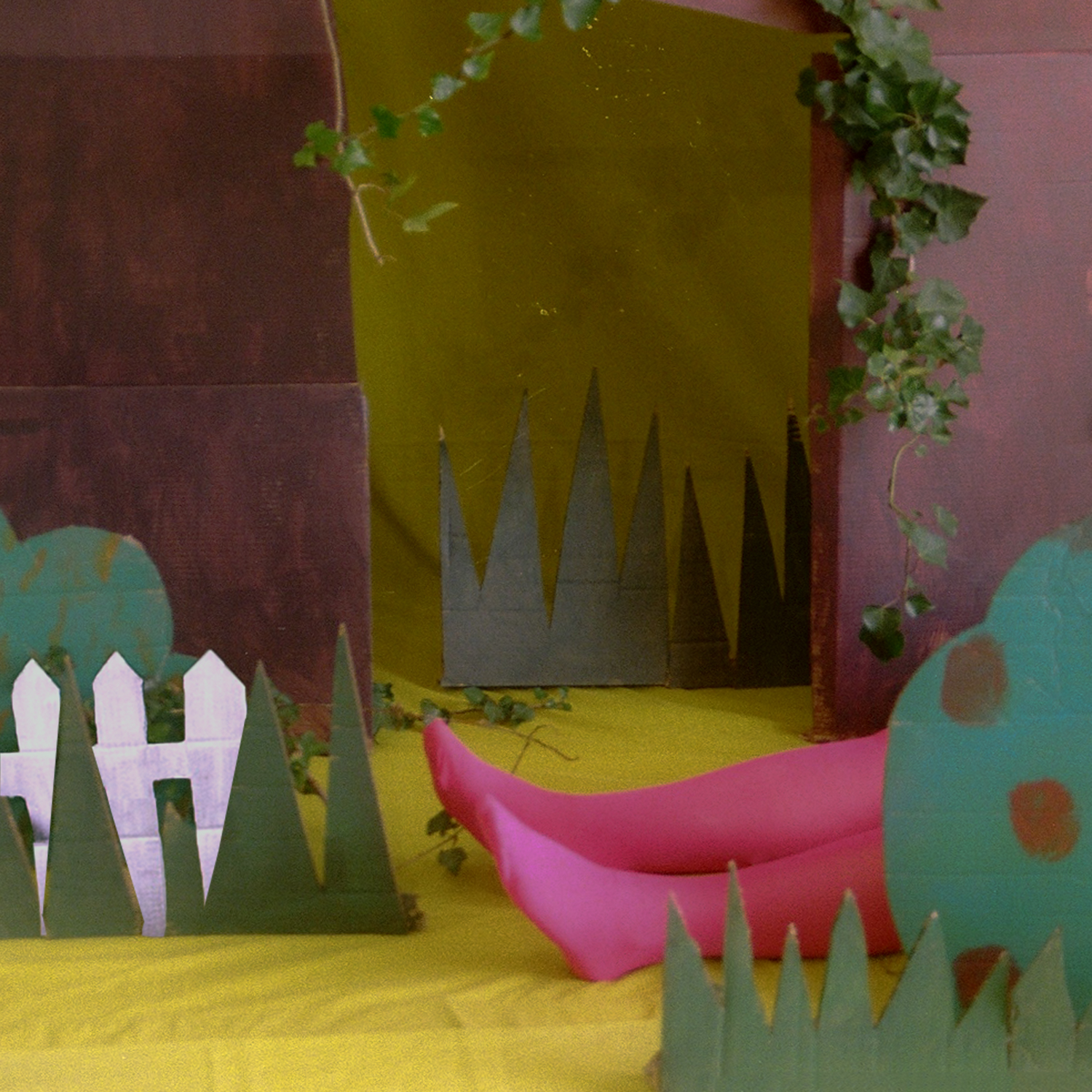 Colour photograph depicting woman's legs in stockings laying on the ground of a cardboard forest. 