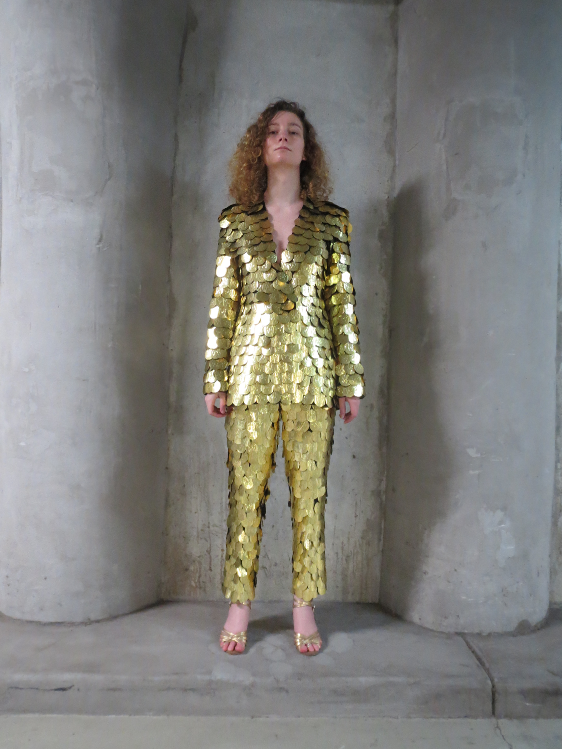 Translucent dissolving suit with red stitching being washed off body by water. Gold scaly sequin covered suit, reflecting daylight and traffic lights.