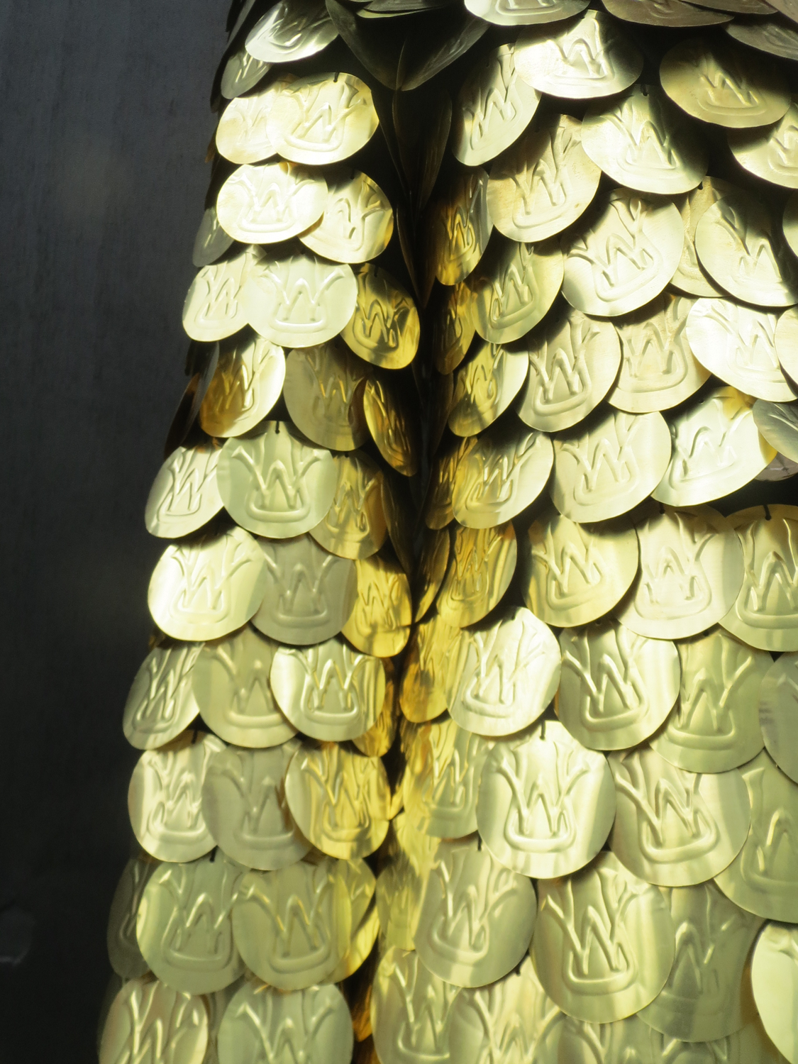 Translucent dissolving suit with red stitching being washed off body by water. Gold scaly sequin covered suit, reflecting daylight and traffic lights.