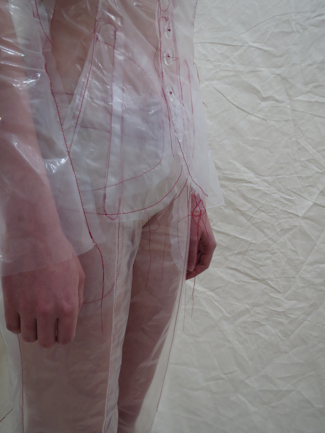 Translucent dissolving suit with red stitching being washed off body by water. Gold scaly sequin covered suit, reflecting daylight and traffic lights.