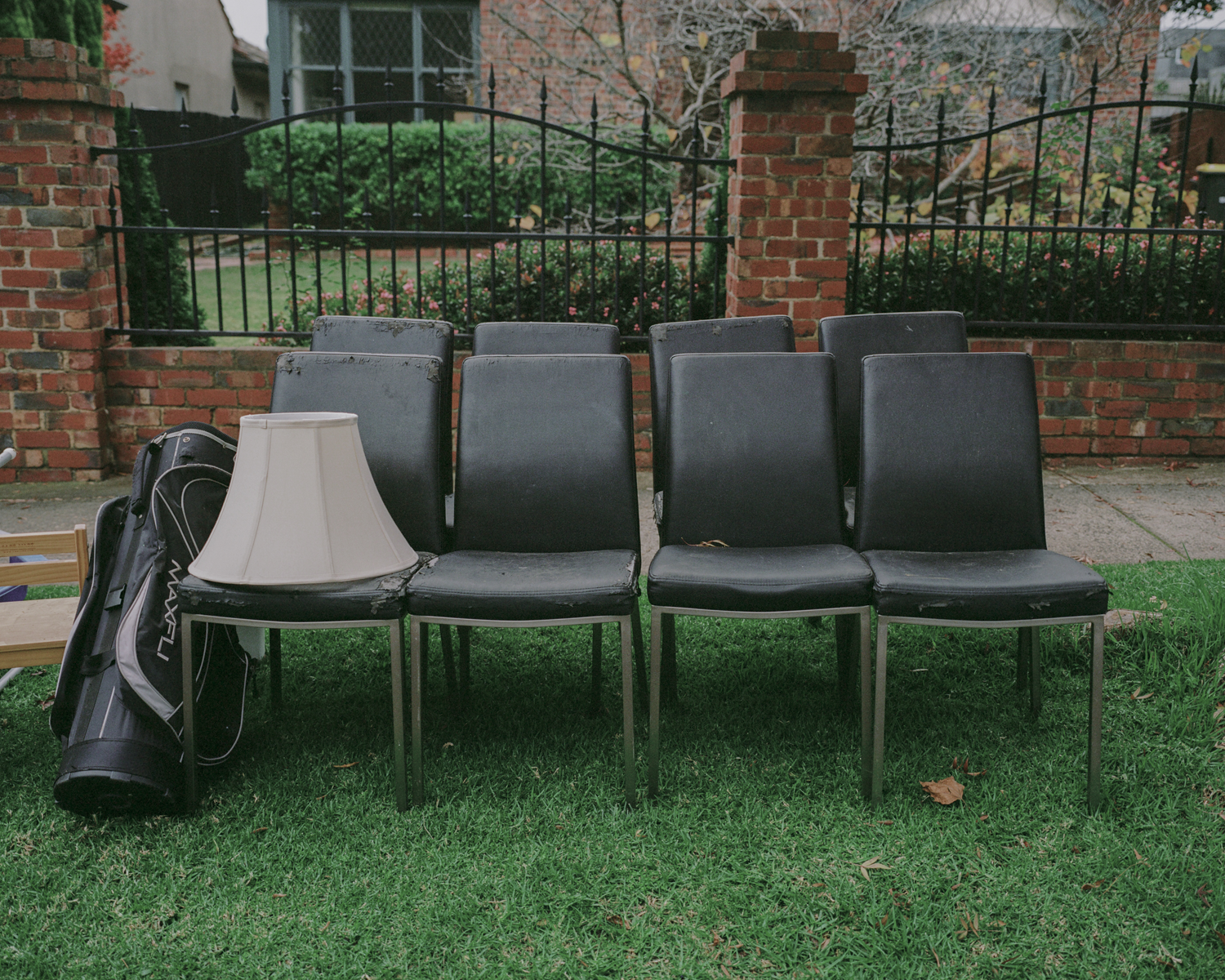 Colour photograph depicting four chairs, a lamp and a golf bag on a nature strip.